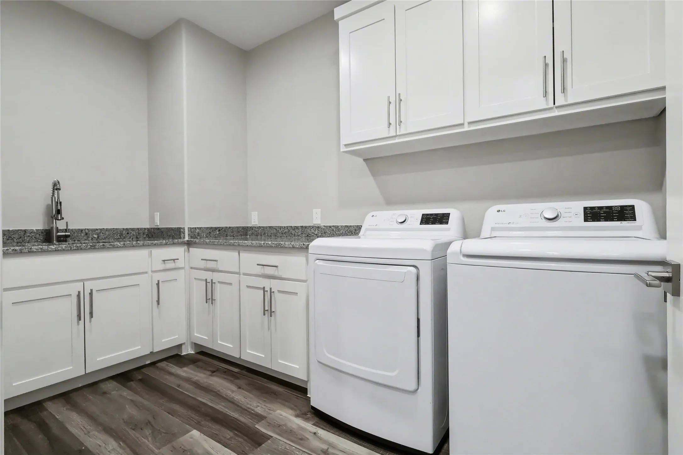 Utility room featuring white cabinetry, granite countertops, and wood-finish flooring