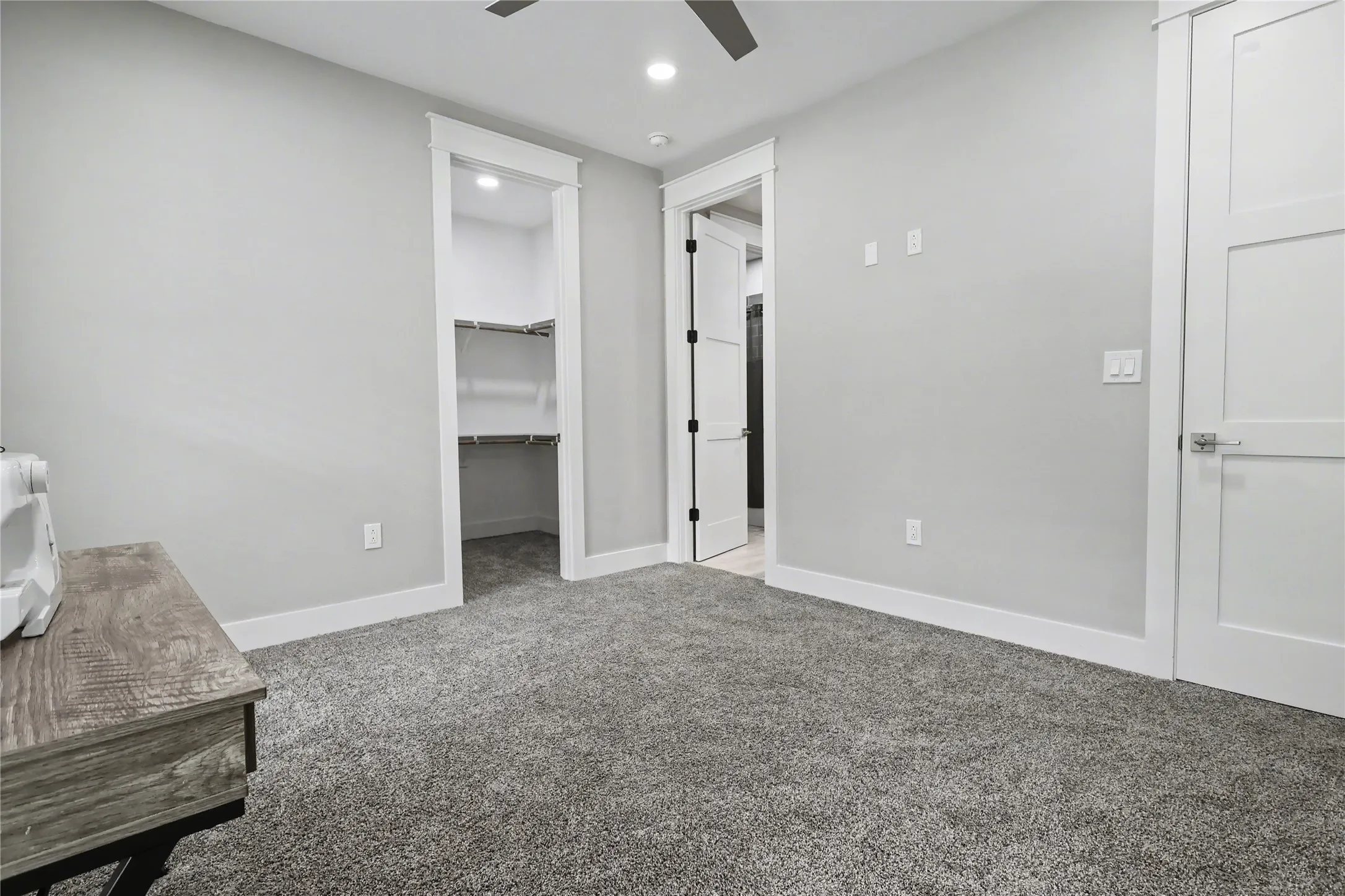 Spacious room featuring plush gray carpeting, crisp white trim, and a built-in closet with shelving