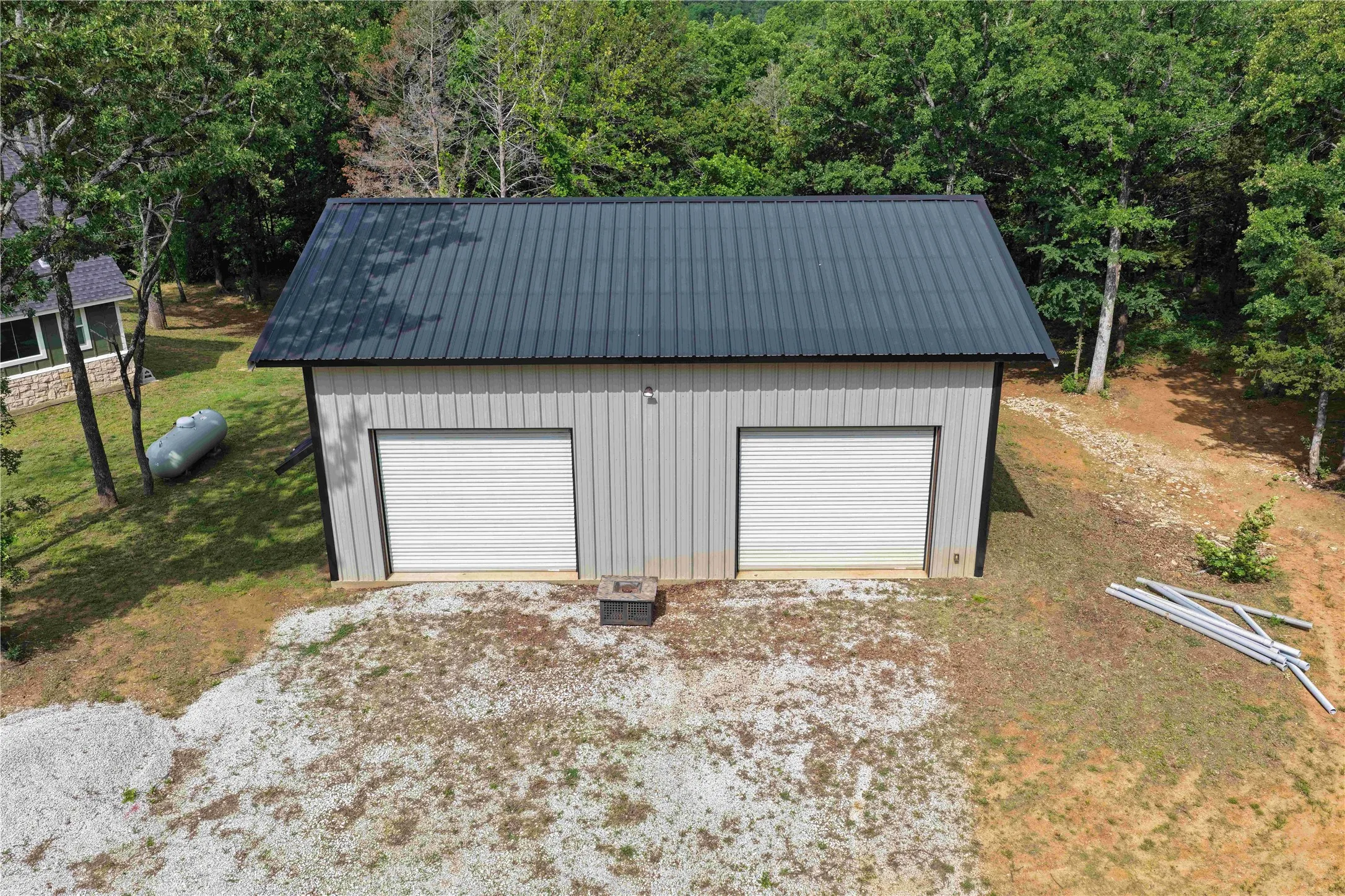 Two-bay garage with a dark metal roof and light-toned vertical siding, featuring two white roll-up doors