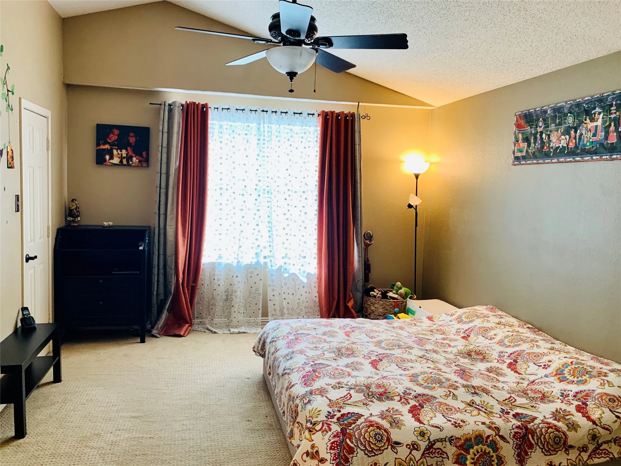 Spacious room featuring vaulted ceilings, a ceiling fan, broad window with natural light, and plush carpeting