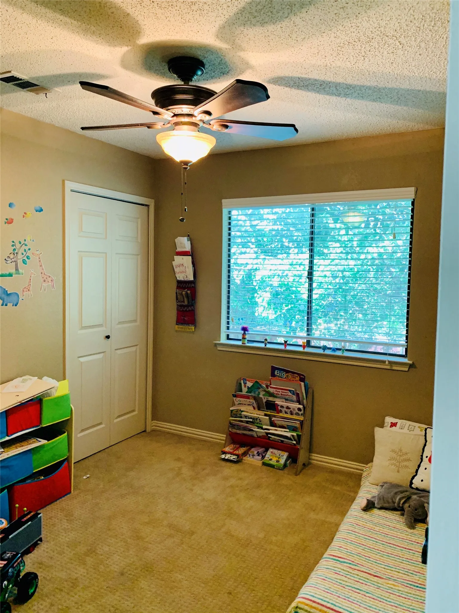 Carpeted room featuring a ceiling fan with integrated lighting, a window with horizontal blinds, and a bi-fold closet door