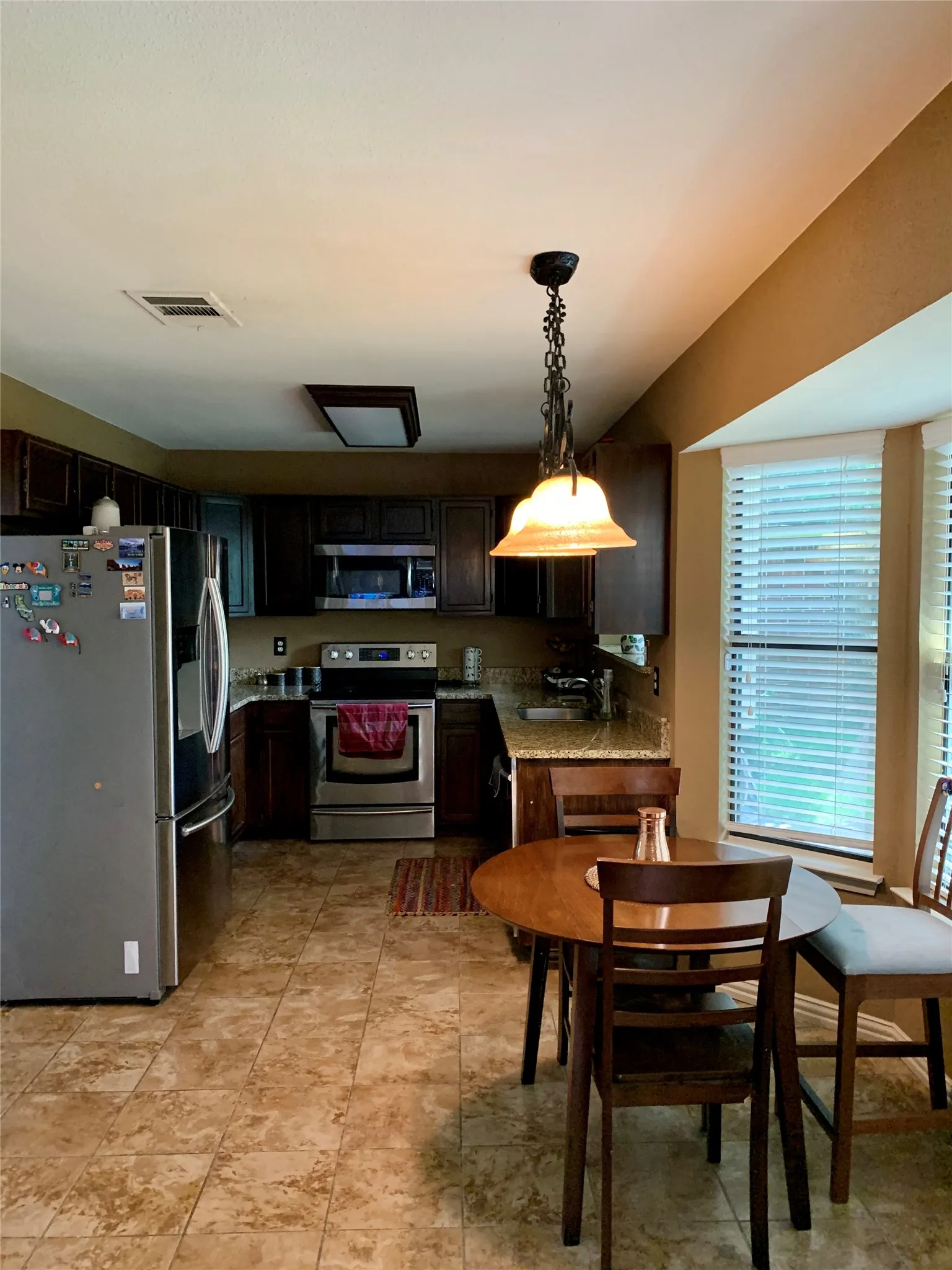 Kitchen featuring stainless steel appliances, dark wood-finish cabinetry, granite countertops, and tiled flooring