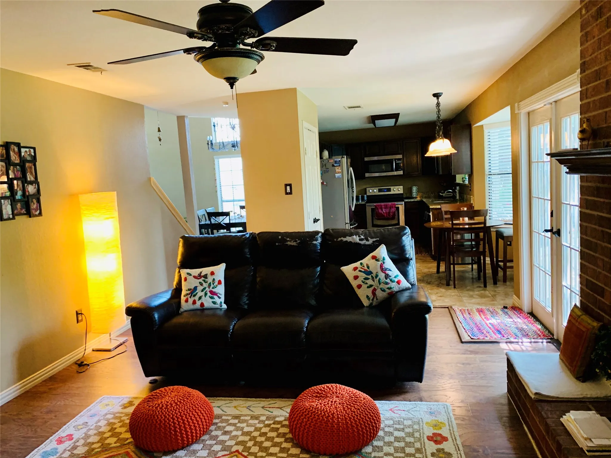 Living area featuring wood-finish flooring, a ceiling fan with integrated lighting, and a brick fireplace surround with a mantel
