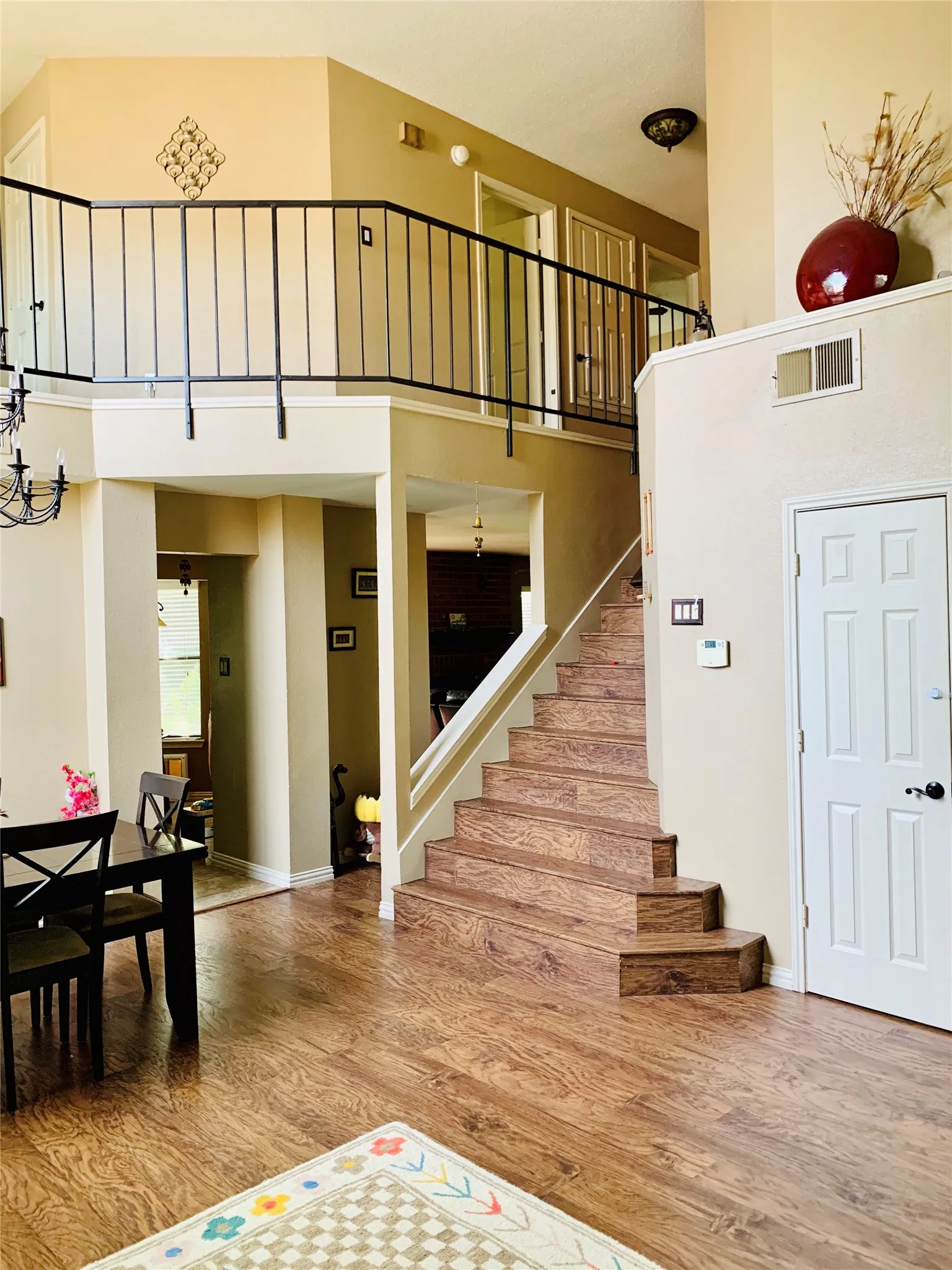 Open-concept interior featuring wood-finish flooring, a prominent staircase with matching wood-finish treads, and a second-story landing framed by a black metal railing
