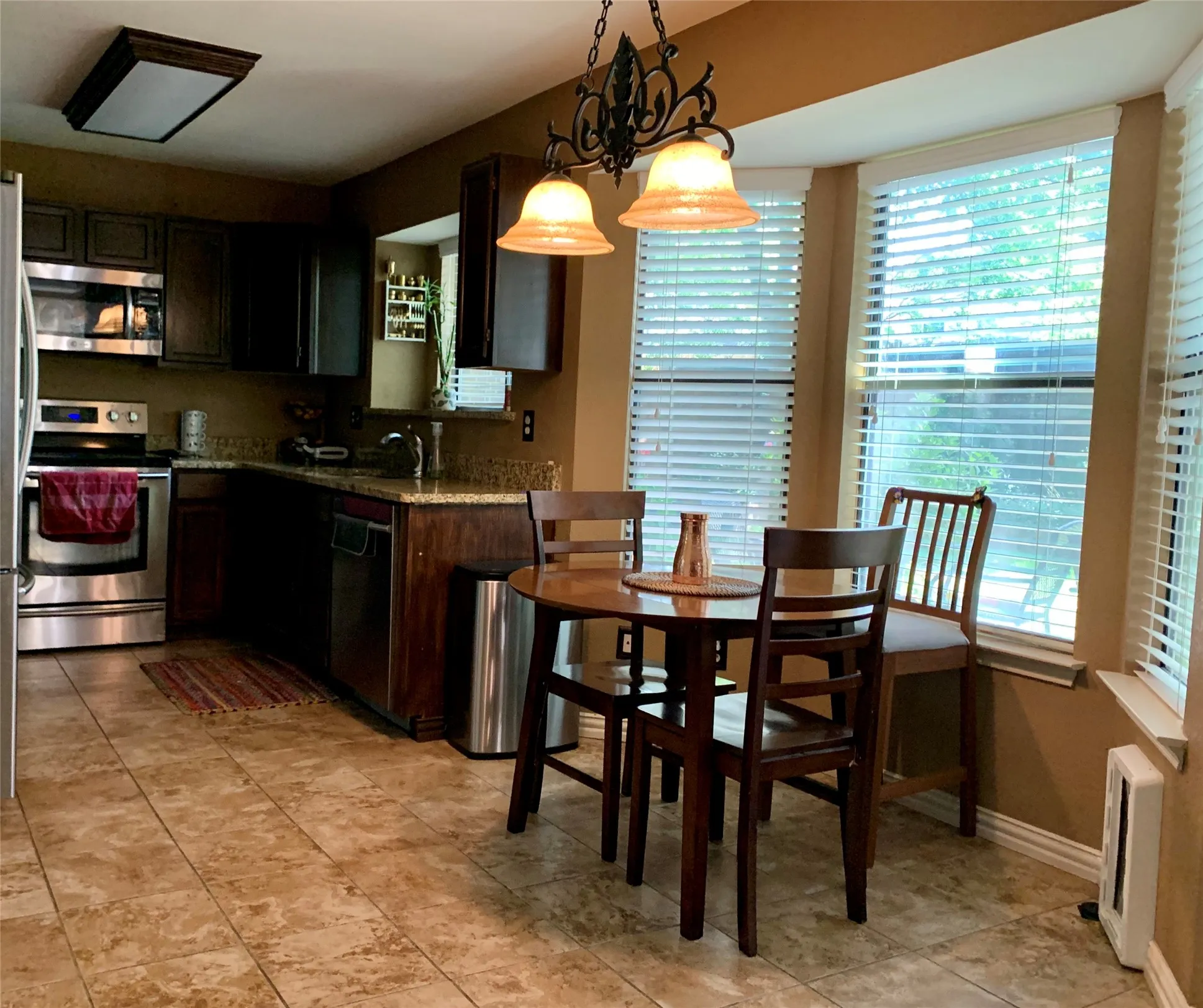 Kitchen featuring stainless steel appliances, dark wood-finish cabinetry, light-toned granite countertops, and tile flooring