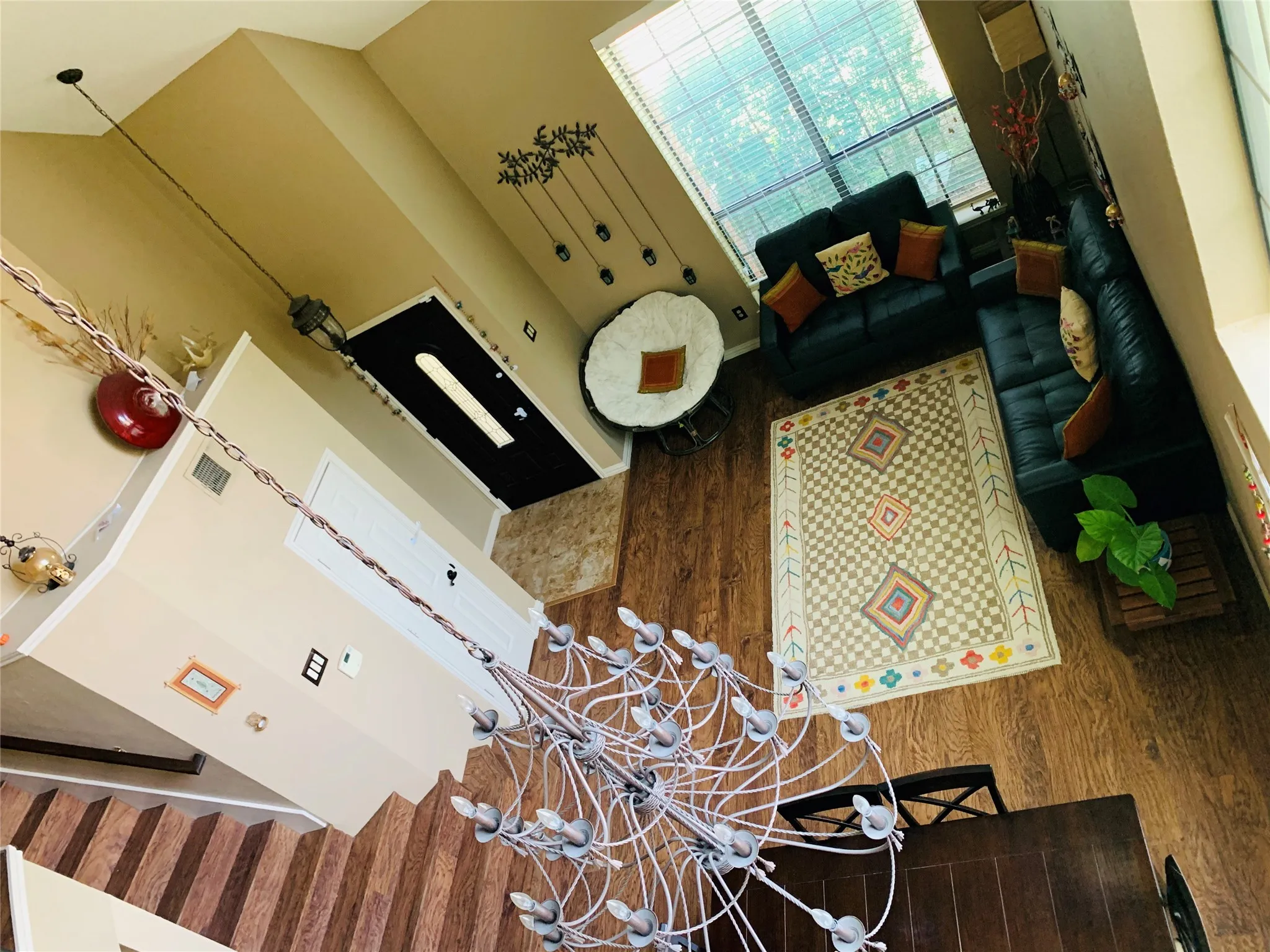 Open-concept living area featuring wood-finish flooring, a large window providing ample natural light, a decorative area rug, and a prominent chandelier