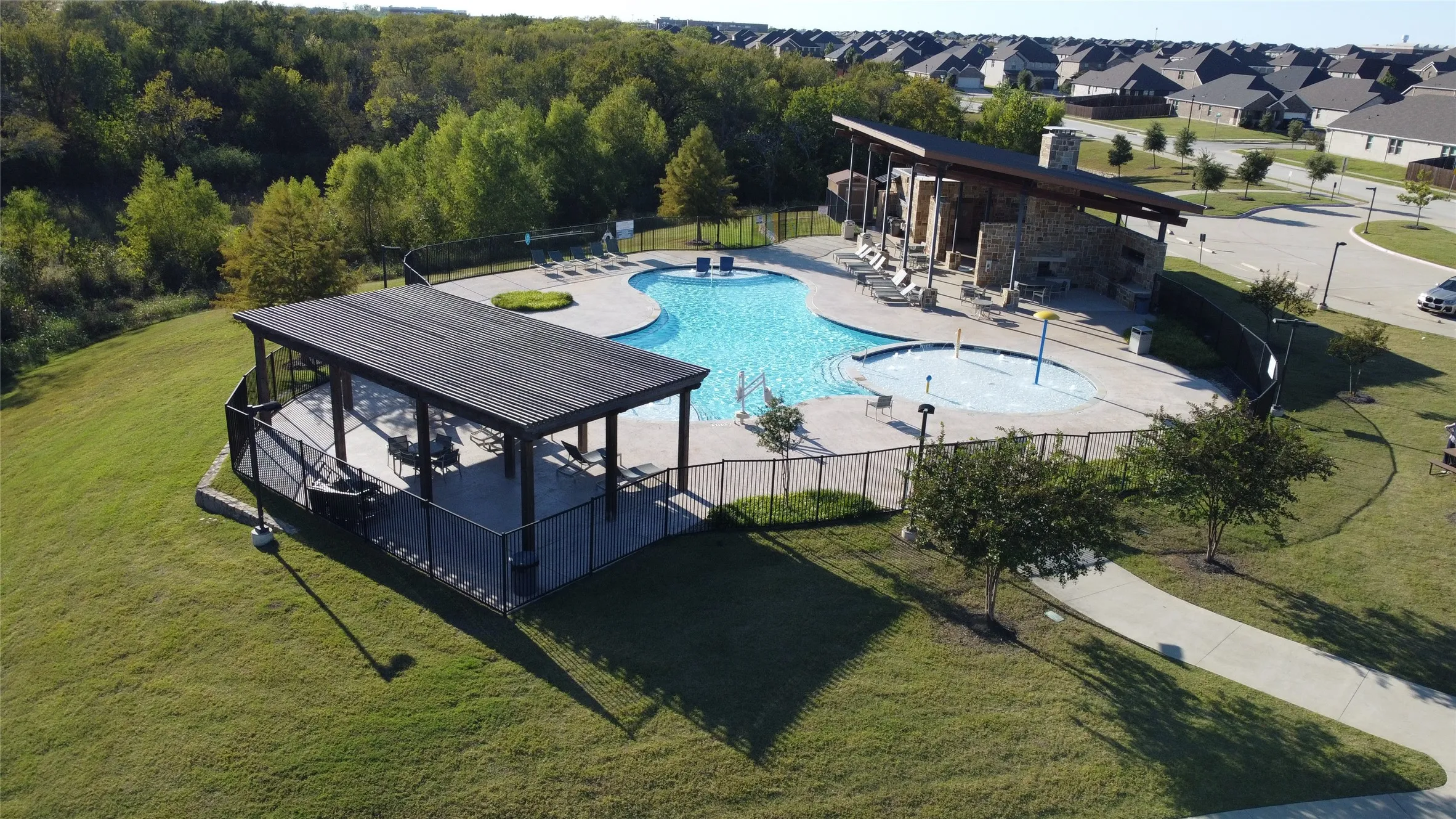 Community pool area featuring a freeform swimming pool, an integrated splash pad, and a stone-clad amenity building with an angular roofline
