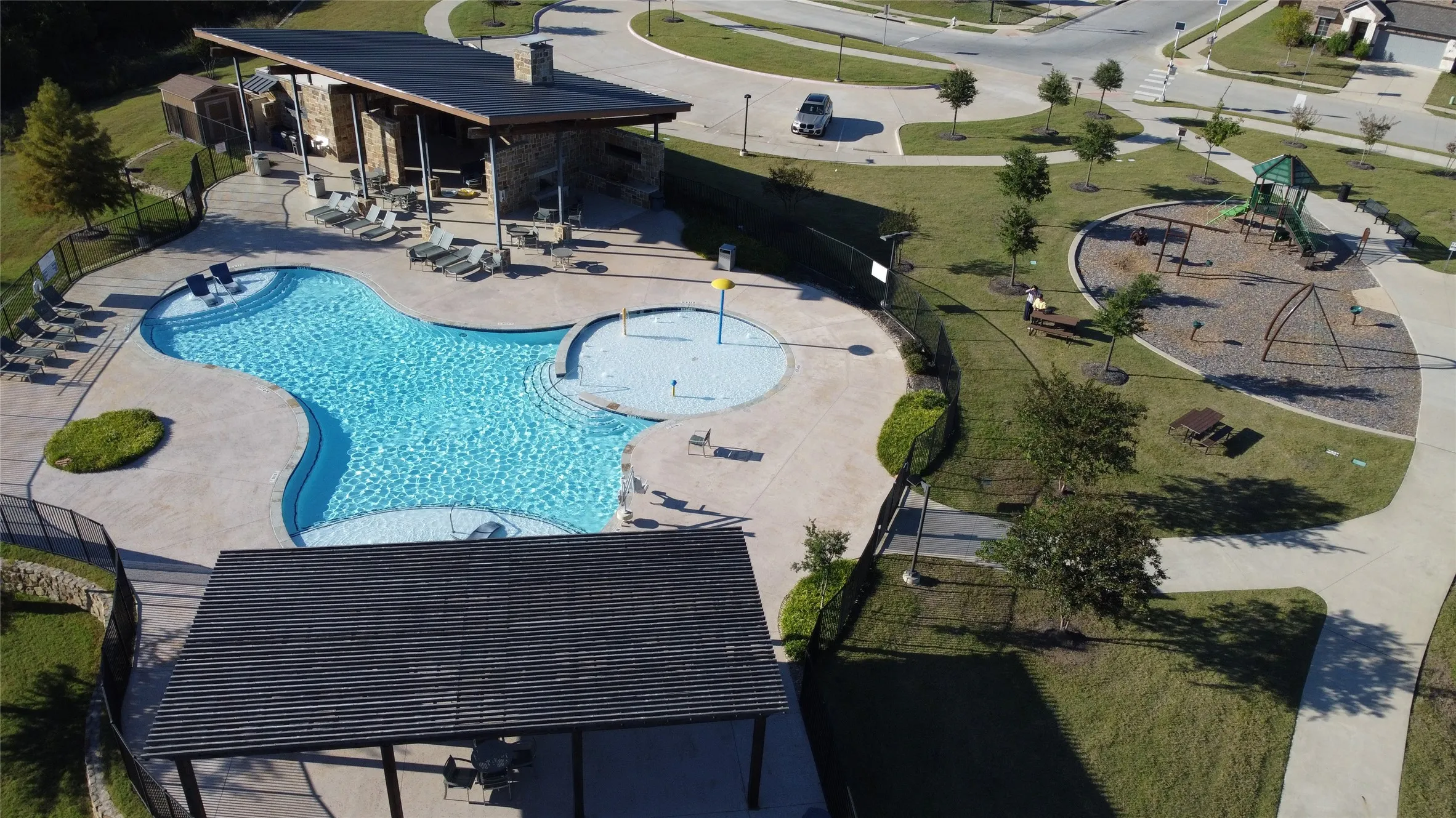 Resort-style pool with integrated splash pad, expansive concrete decking, and covered lounge area