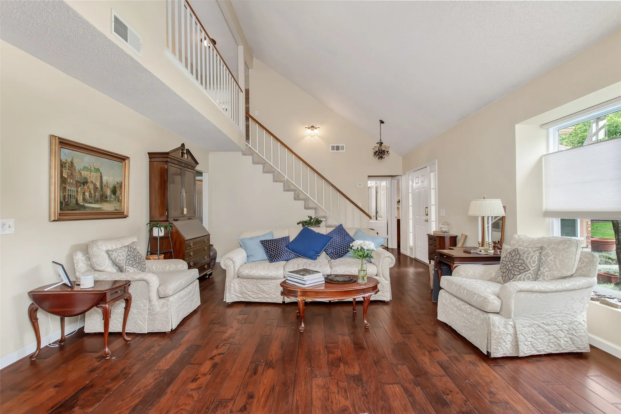 Spacious living area featuring wood-finish flooring, vaulted ceilings, and a prominent staircase with a white railing