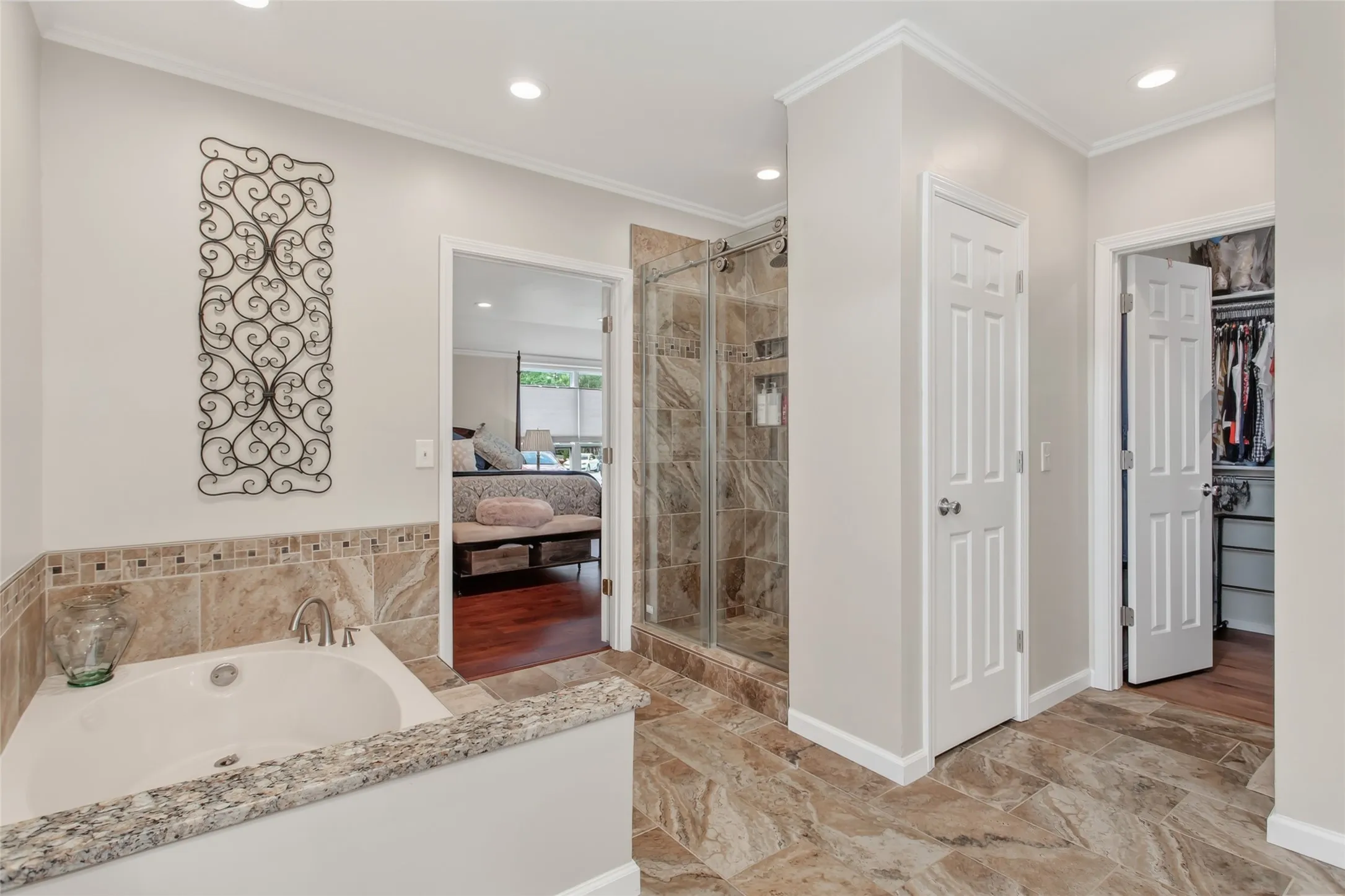 Spacious bathroom featuring a built-in soaking tub with a stone-finish surround, a glass-enclosed shower, and large format tile flooring