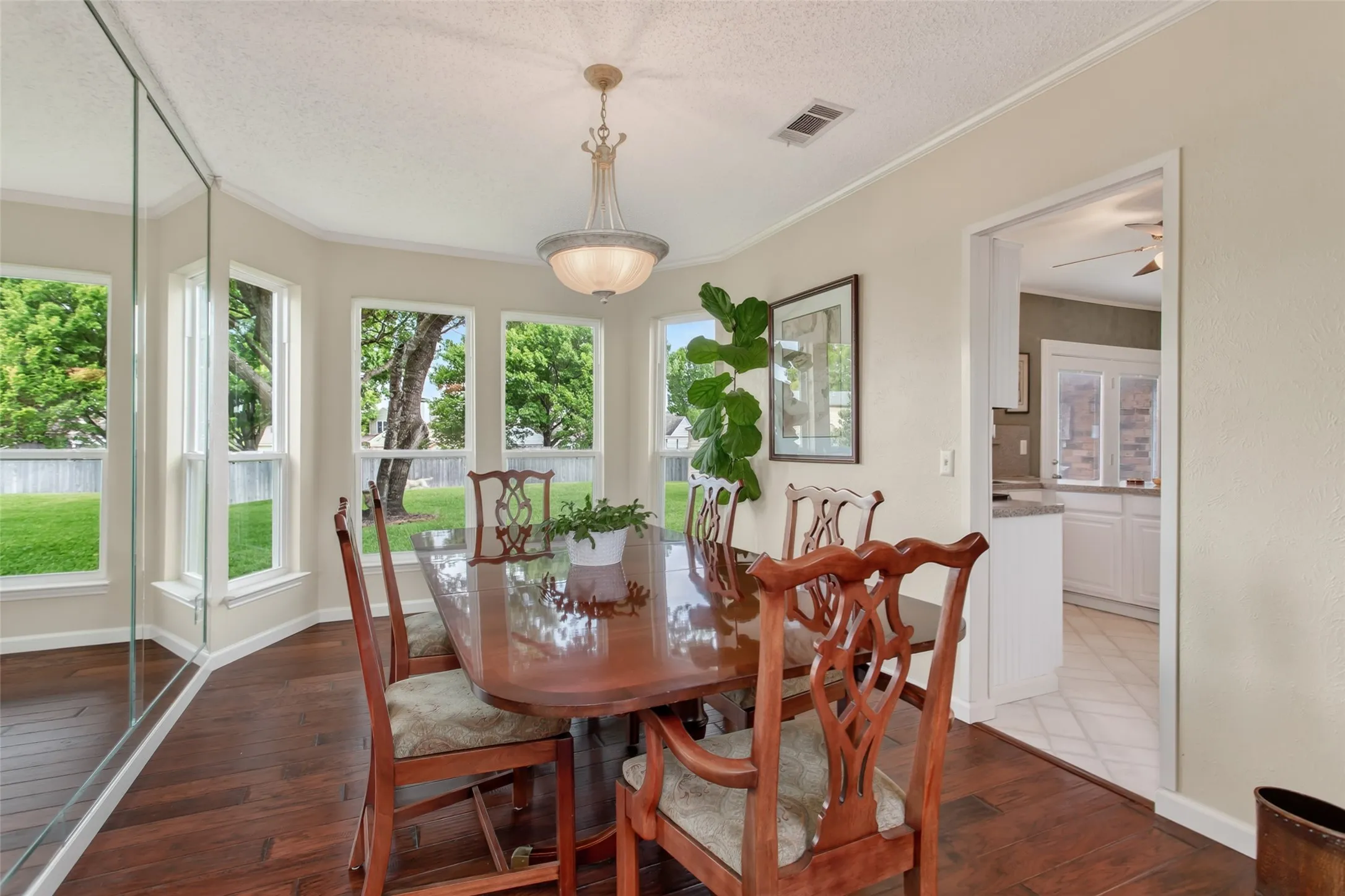 Dining area featuring wood-finish flooring, a bay window with multiple panes, a semi-flush mount chandelier, and a mirrored wall