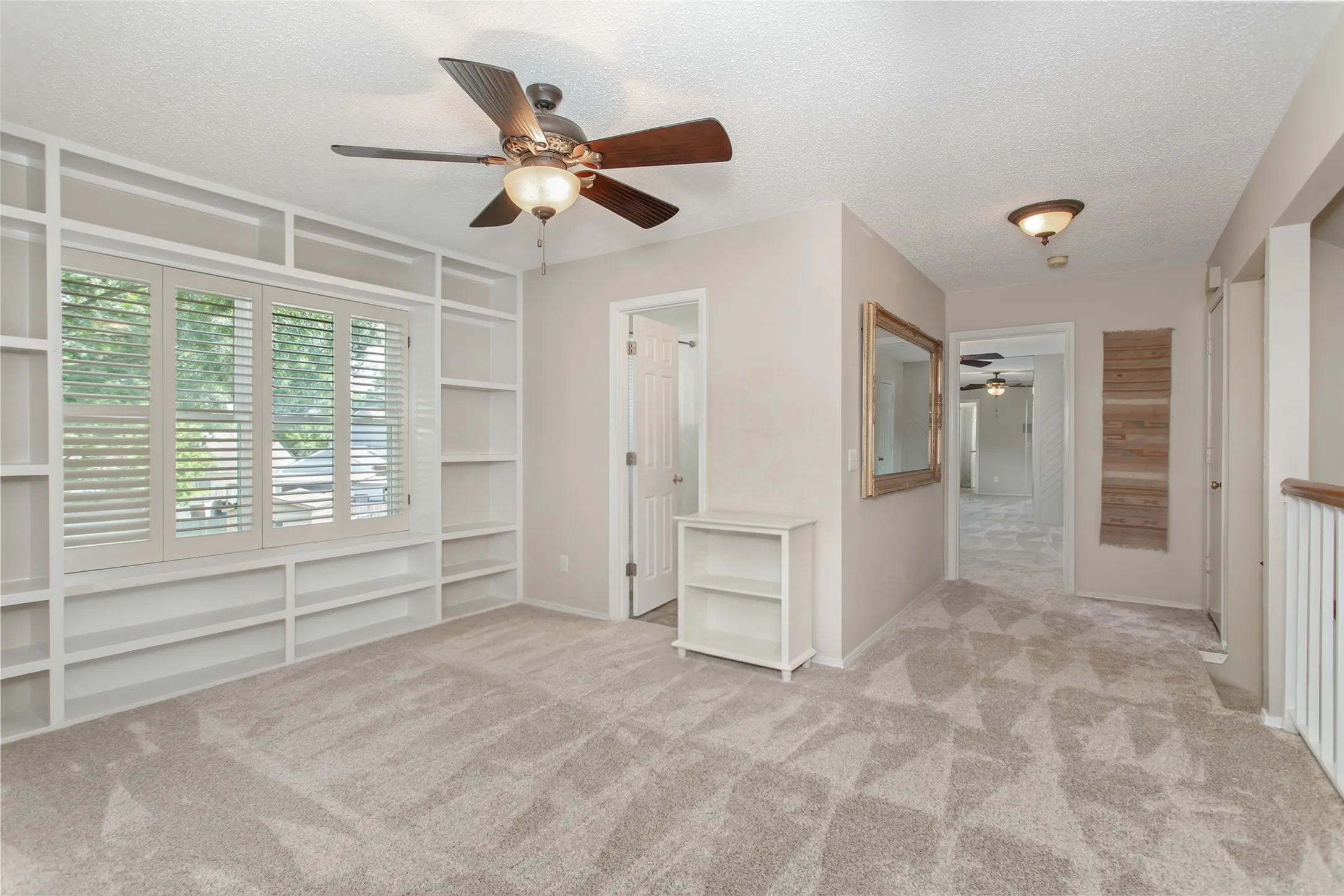 Room featuring extensive built-in shelving, a window with plantation shutters, a ceiling fan with integrated lighting, and neutral-toned carpeting