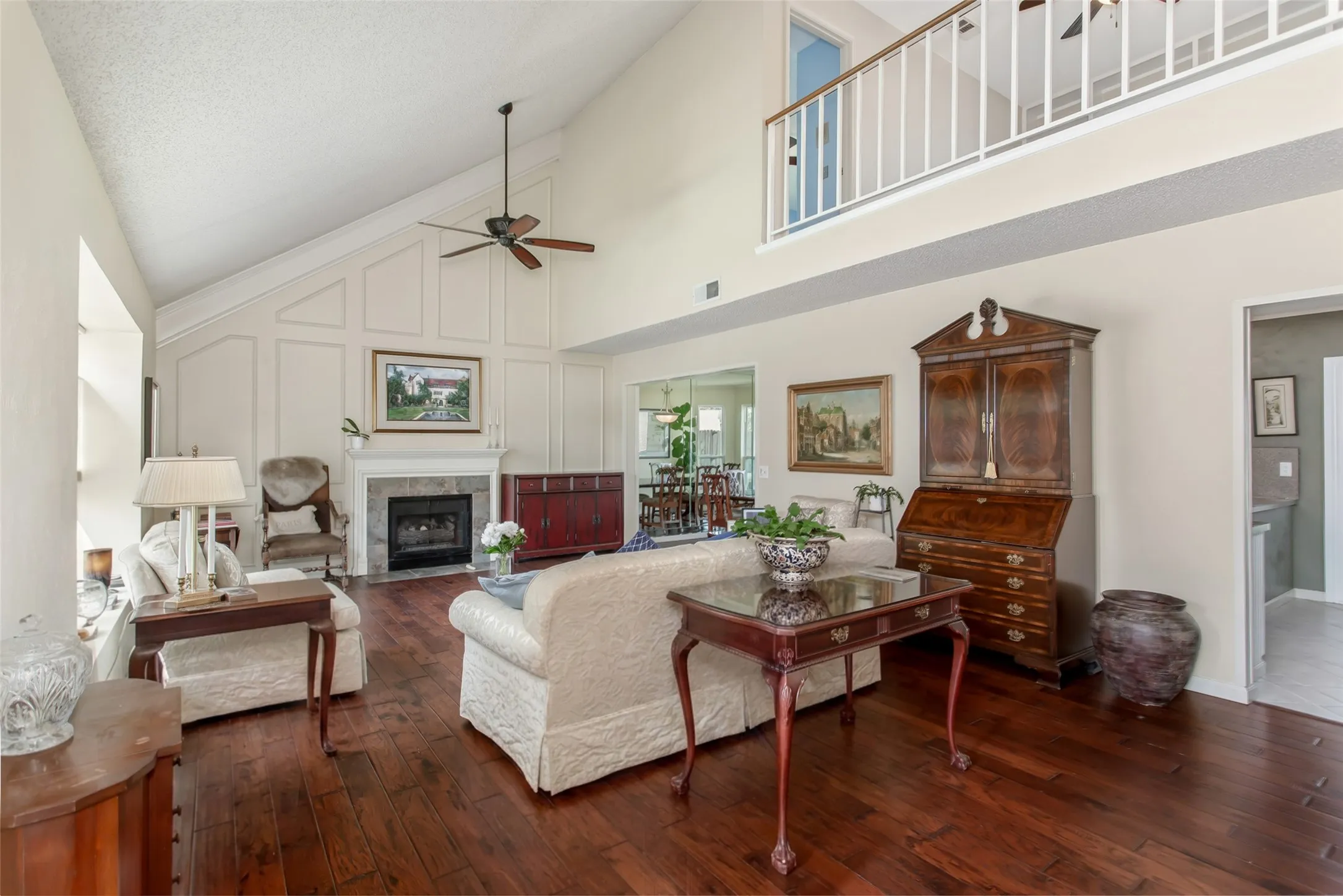 Living area featuring high vaulted ceilings, wood-finish flooring, a fireplace with a stone surround, and a ceiling fan