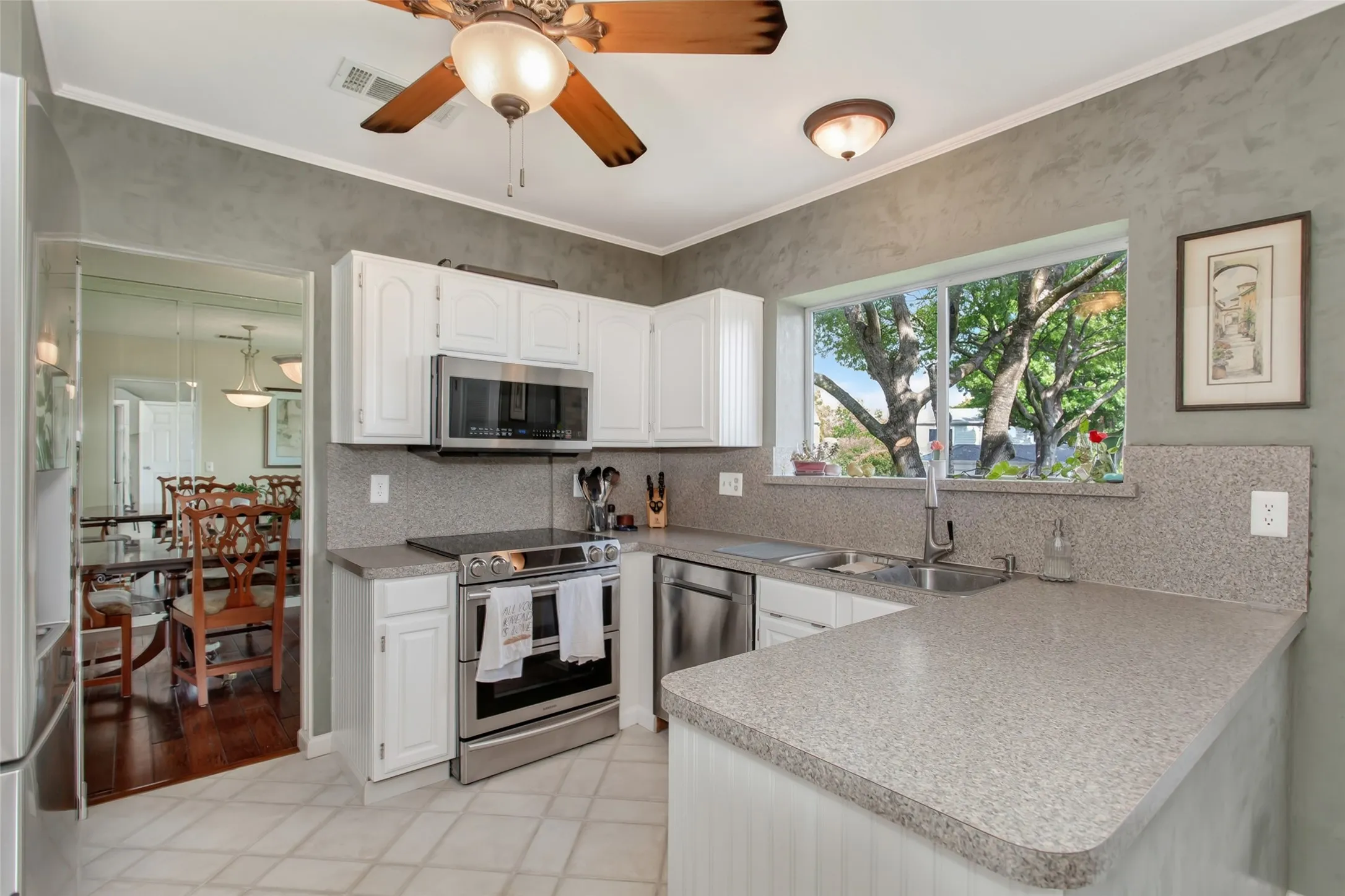 U-shaped kitchen featuring white cabinetry, stainless steel appliances, a window above the sink, and a ceiling fan with integrated lighting