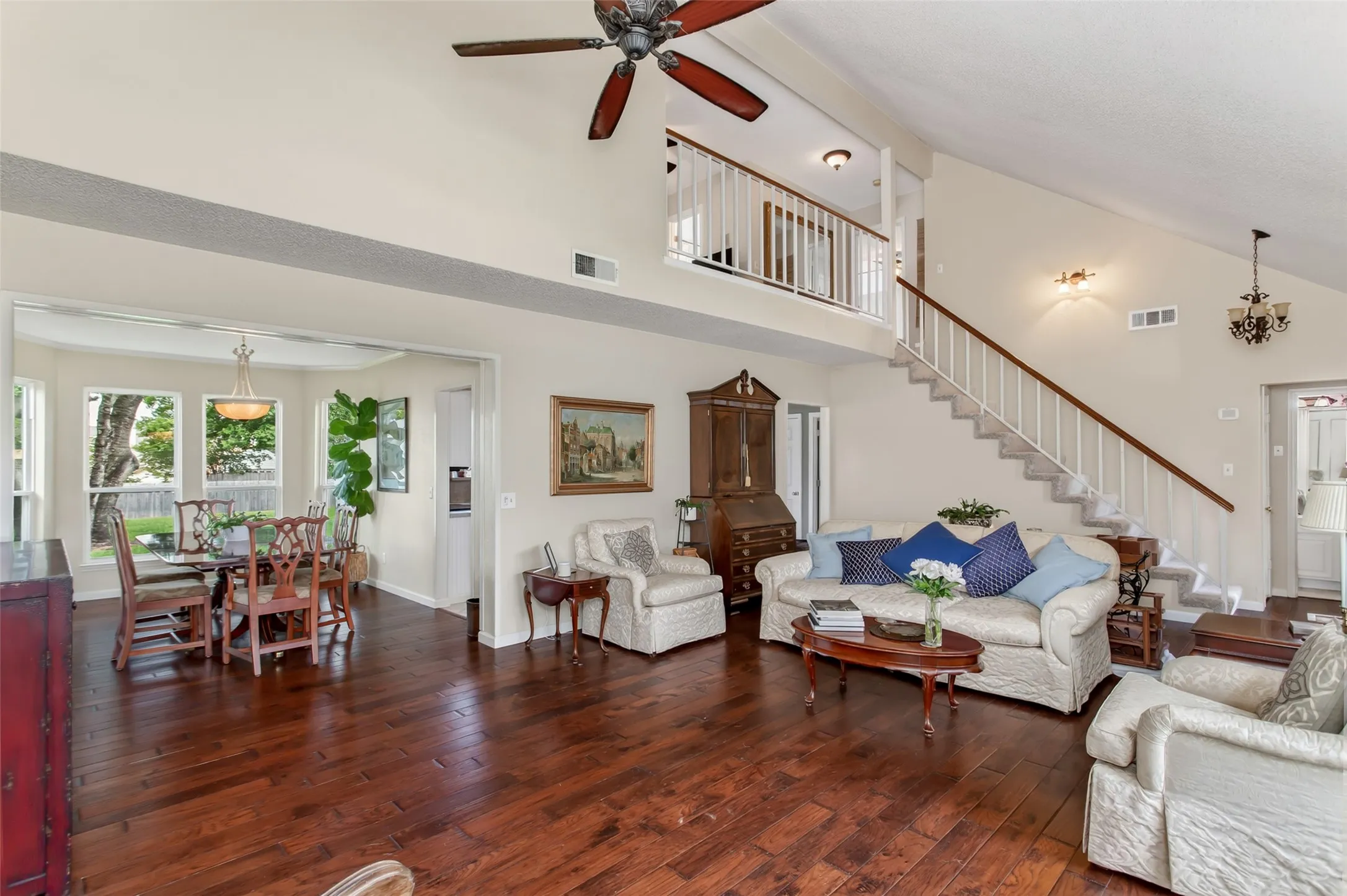 Spacious living area featuring wood-finish flooring, a vaulted ceiling, and a ceiling fan