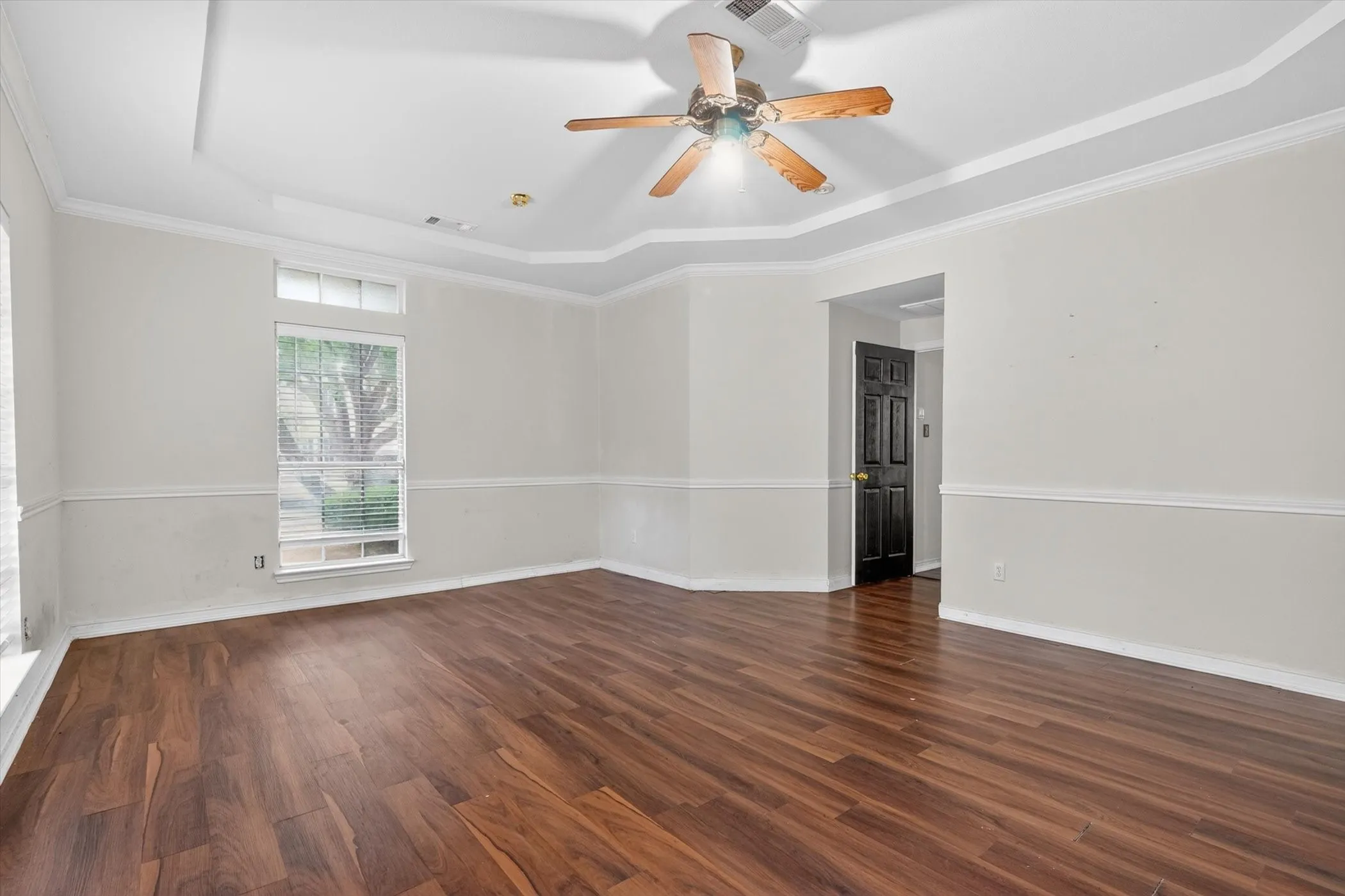 Spacious room featuring wood-finish flooring, a tray ceiling, and a ceiling fan with integrated lighting
