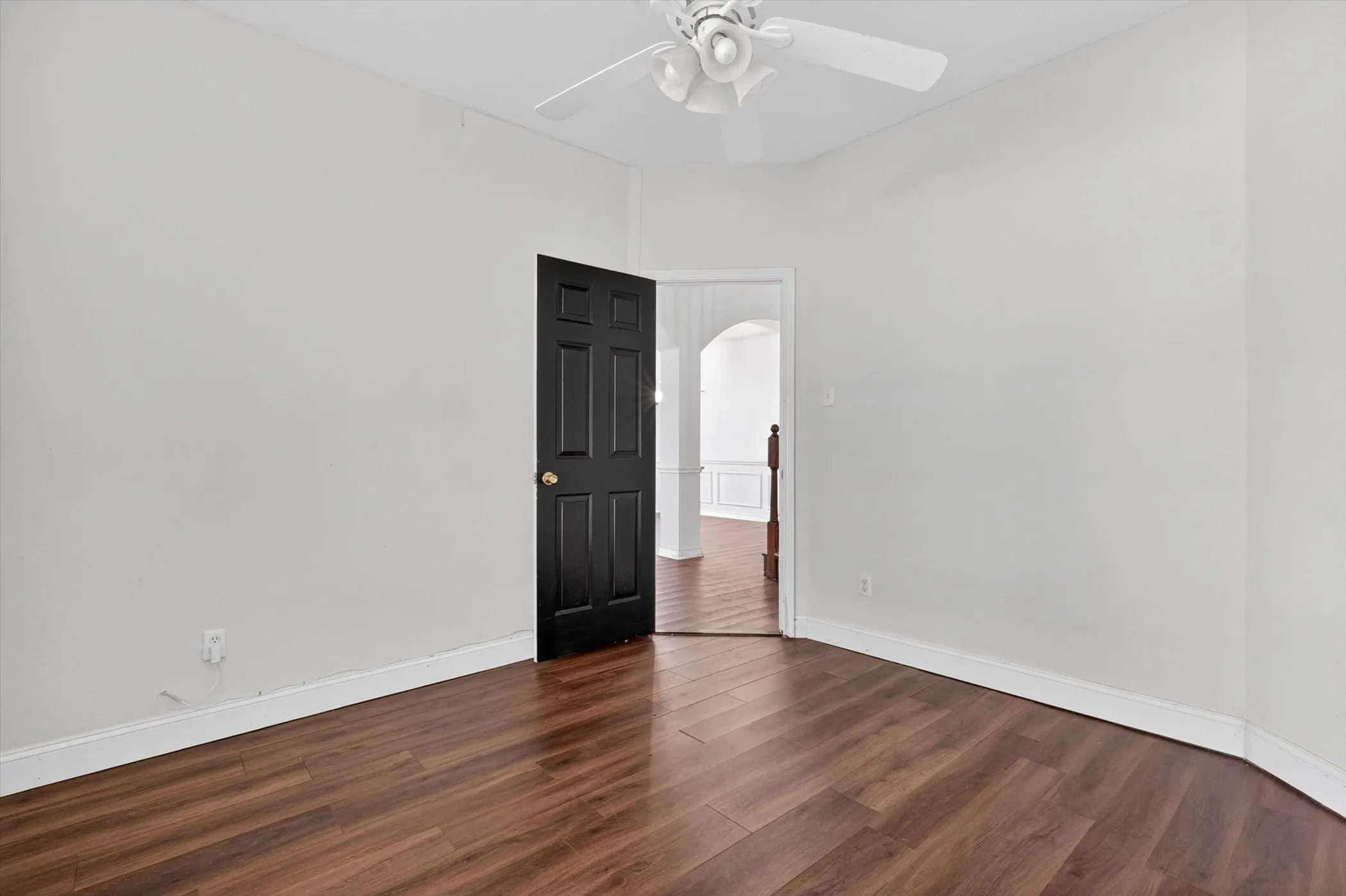 Room featuring wood-finish flooring, white walls, and a ceiling fan with light fixture