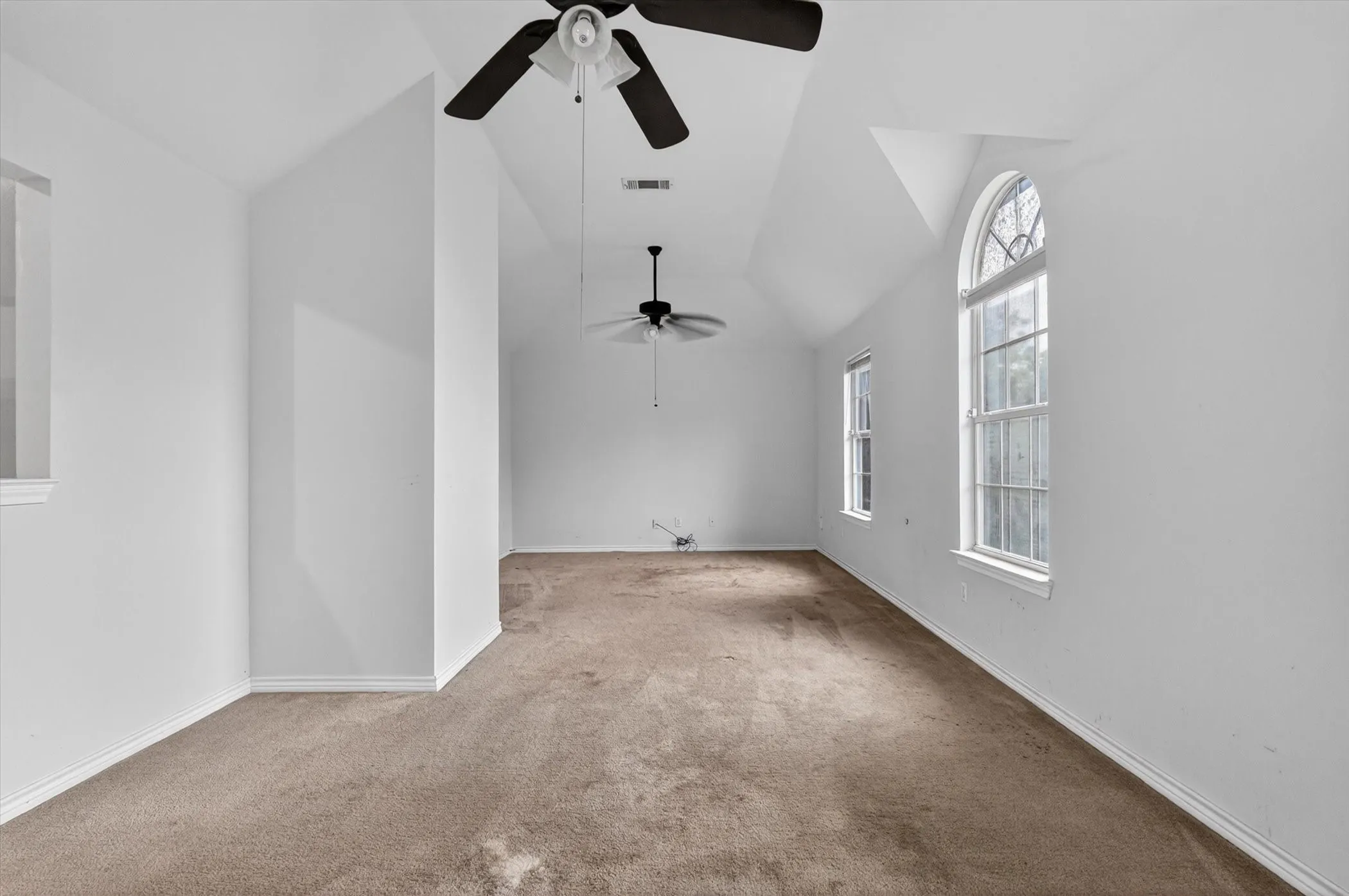 Spacious room featuring a vaulted ceiling and two ceiling fans