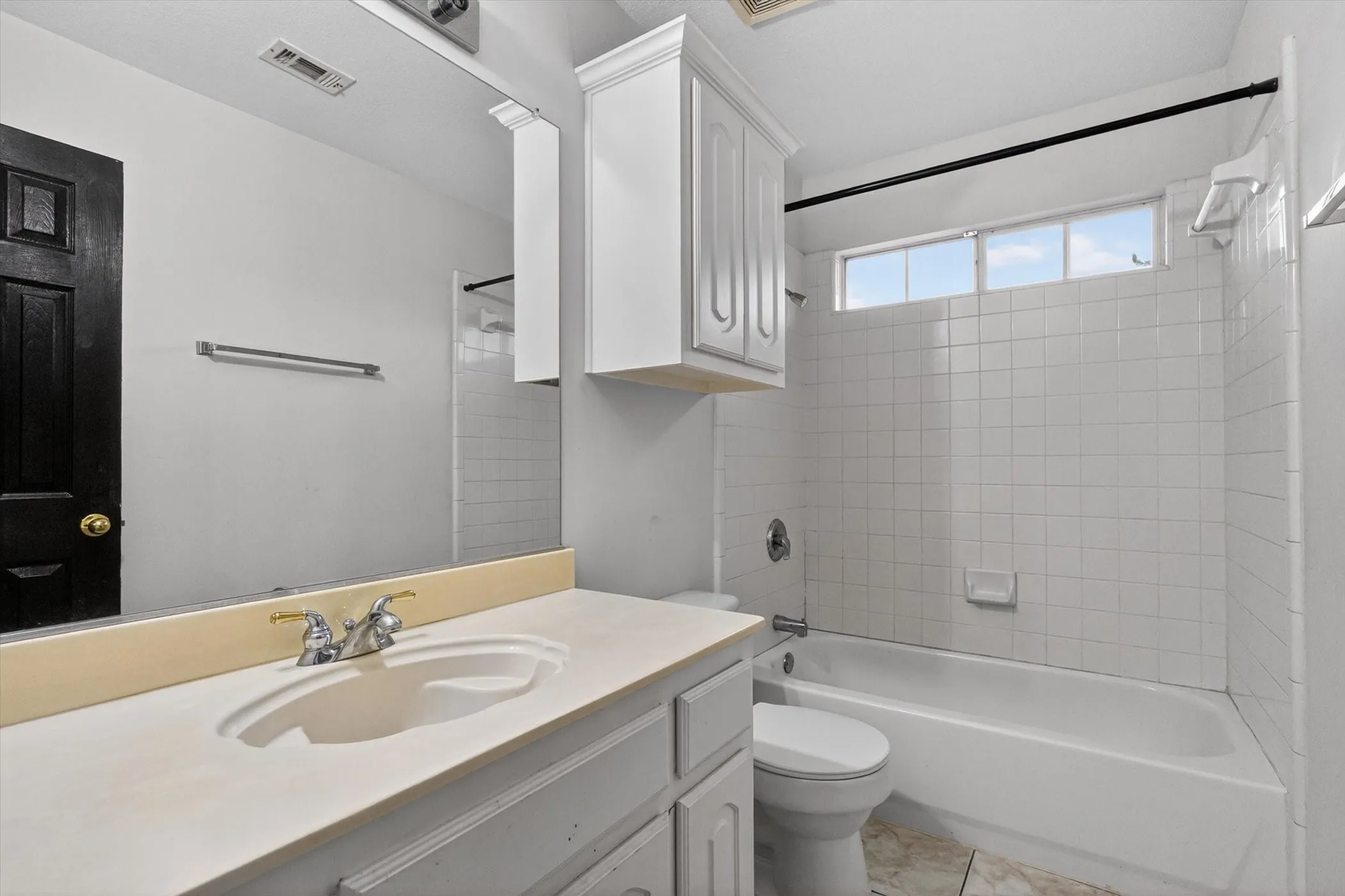 Bathroom featuring a vanity with an integrated sink, a white bathtub with tile surround, and a high transom window