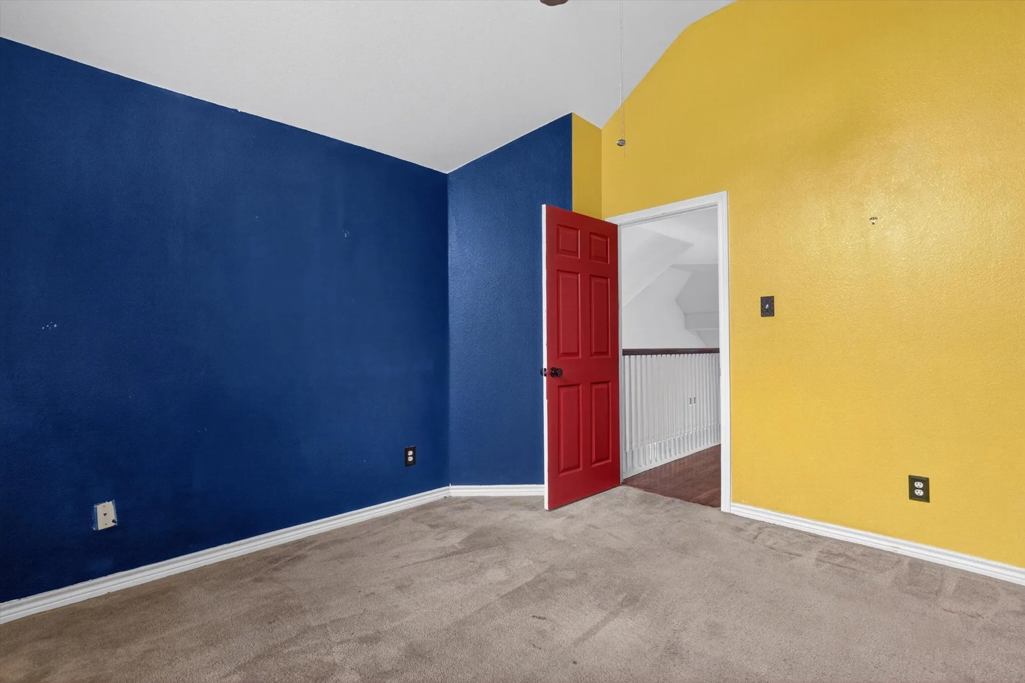 Carpeted room featuring a red six-panel door, white trim, and a vaulted ceiling