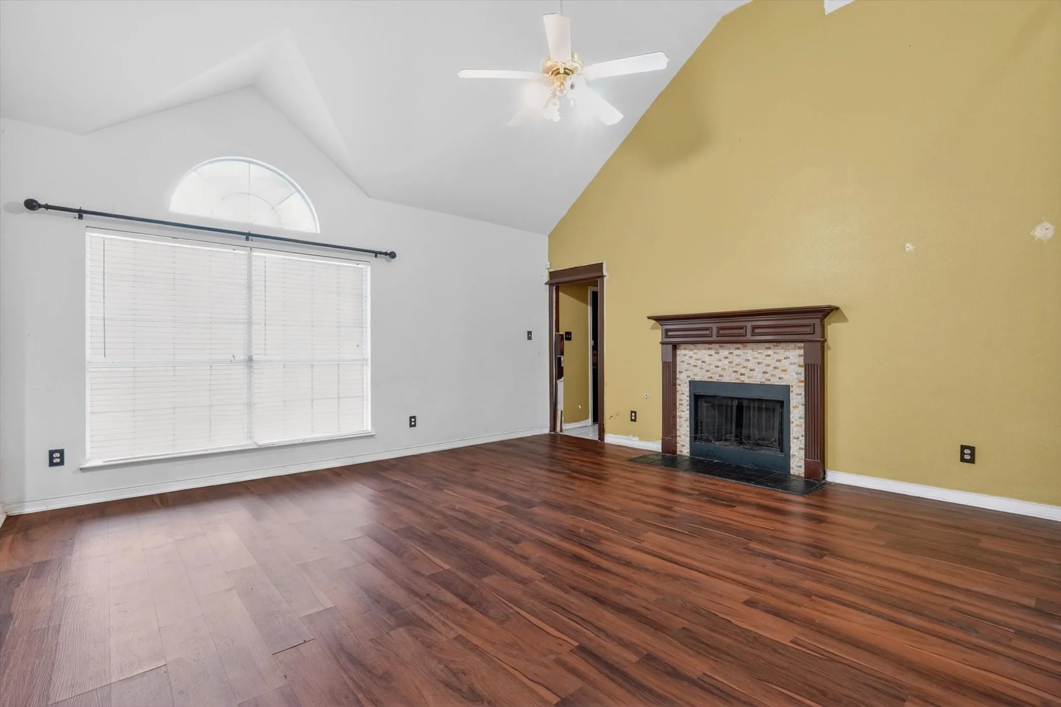 Spacious living area featuring wood-finish flooring, a vaulted ceiling, and a ceiling fan