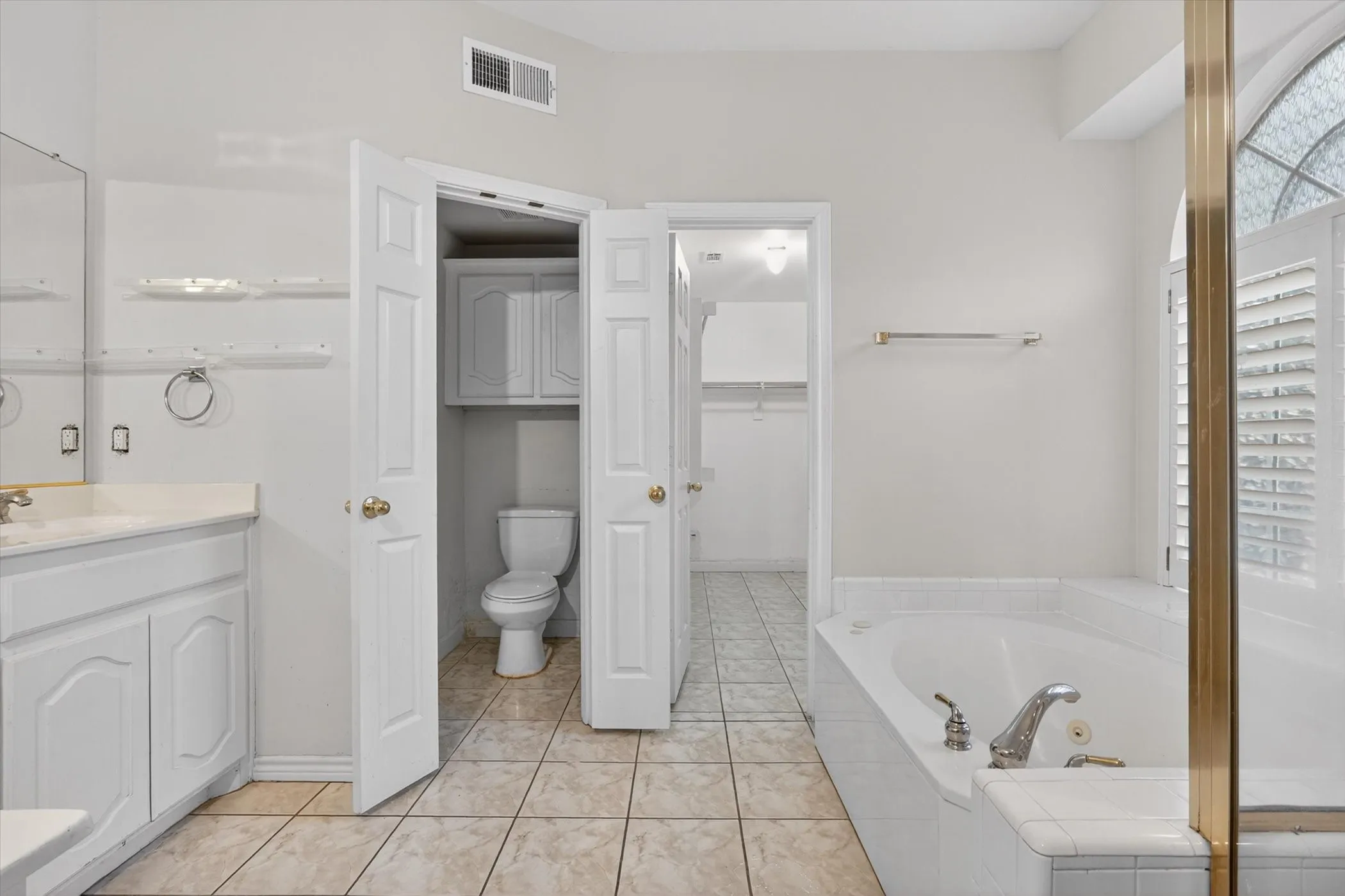 Bathroom featuring a built-in tub with tile surround, a single vanity with stone-finish countertop, and a water closet with built-in cabinetry