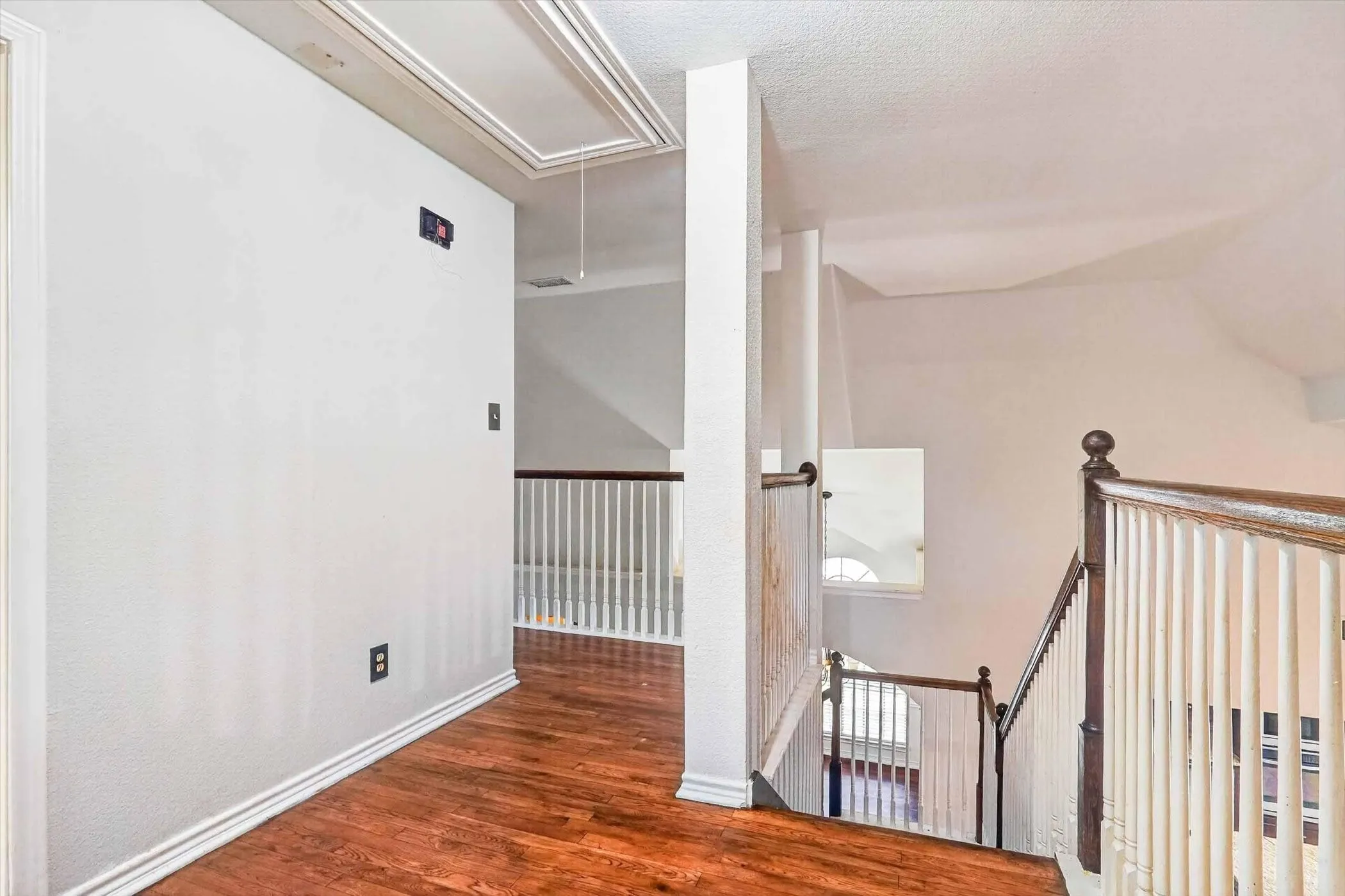 Upper-level hallway featuring rich wood-finish flooring, white baseboards, and a white baluster railing with a wooden handrail