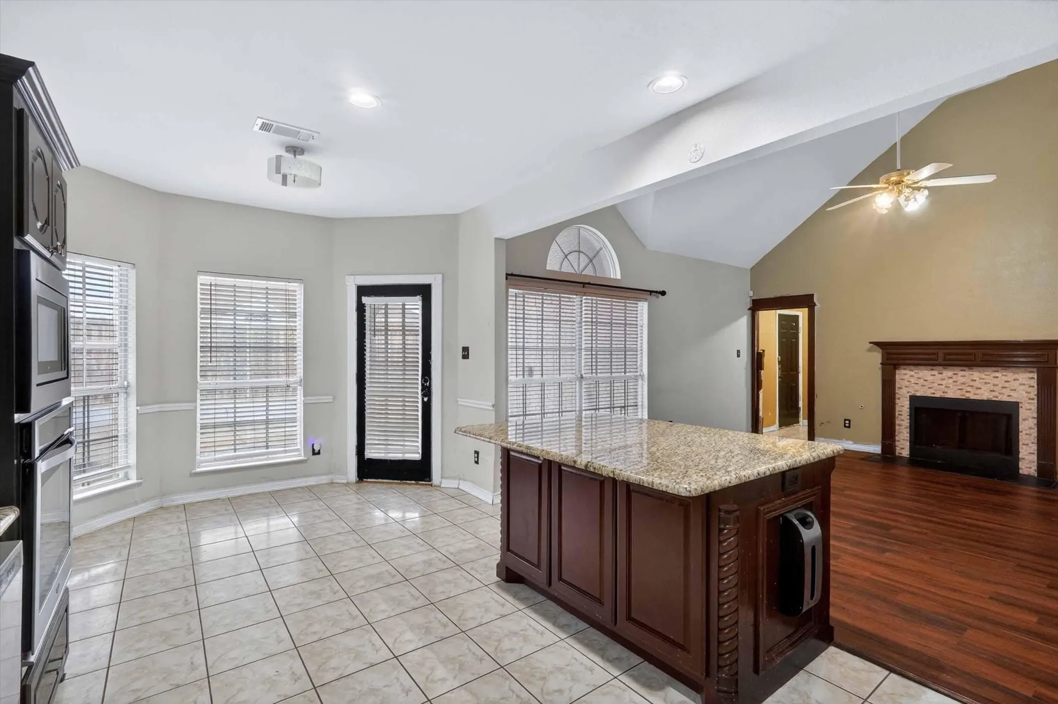 Spacious kitchen with tile flooring, a granite-topped island with carved wood detailing, and built-in black appliances