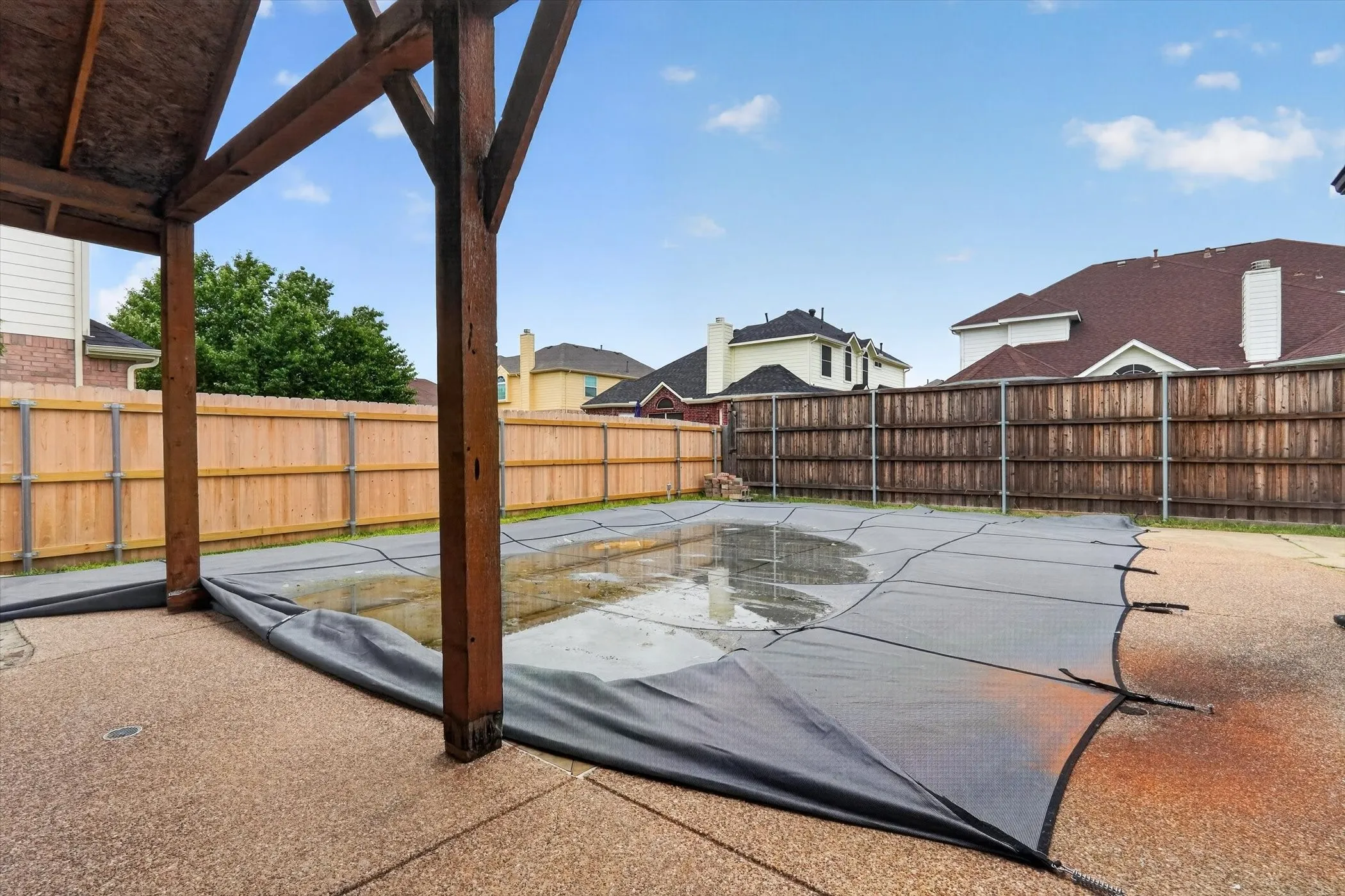 Covered pool area featuring a wooden pergola, aggregate concrete patio, and perimeter wood fencing