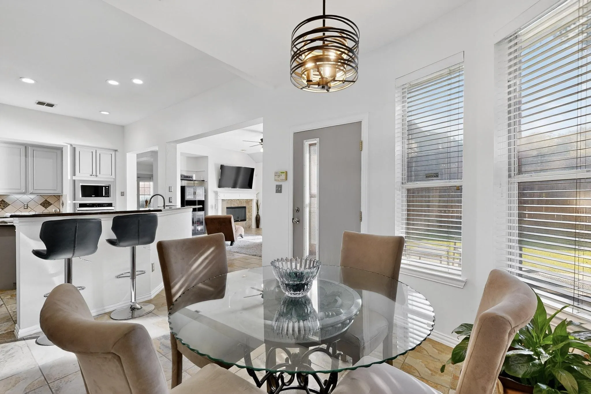 Bright dining area featuring a glass-top table, neutral upholstered chairs, and a contemporary chandelier