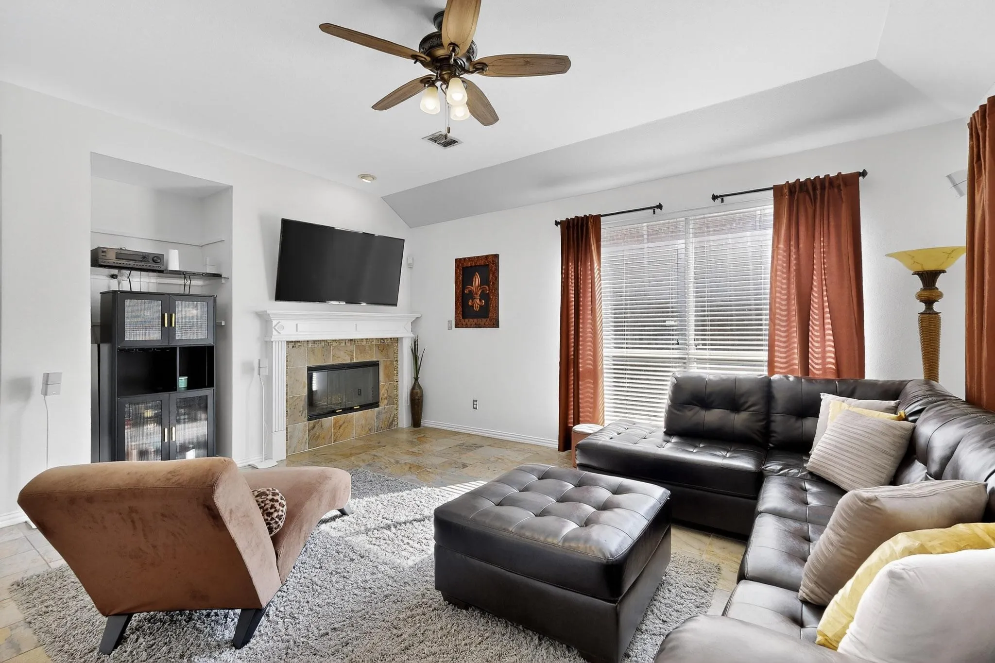 Living area featuring a fireplace with stone surround and white mantel, vaulted ceiling with a ceiling fan, and tile flooring