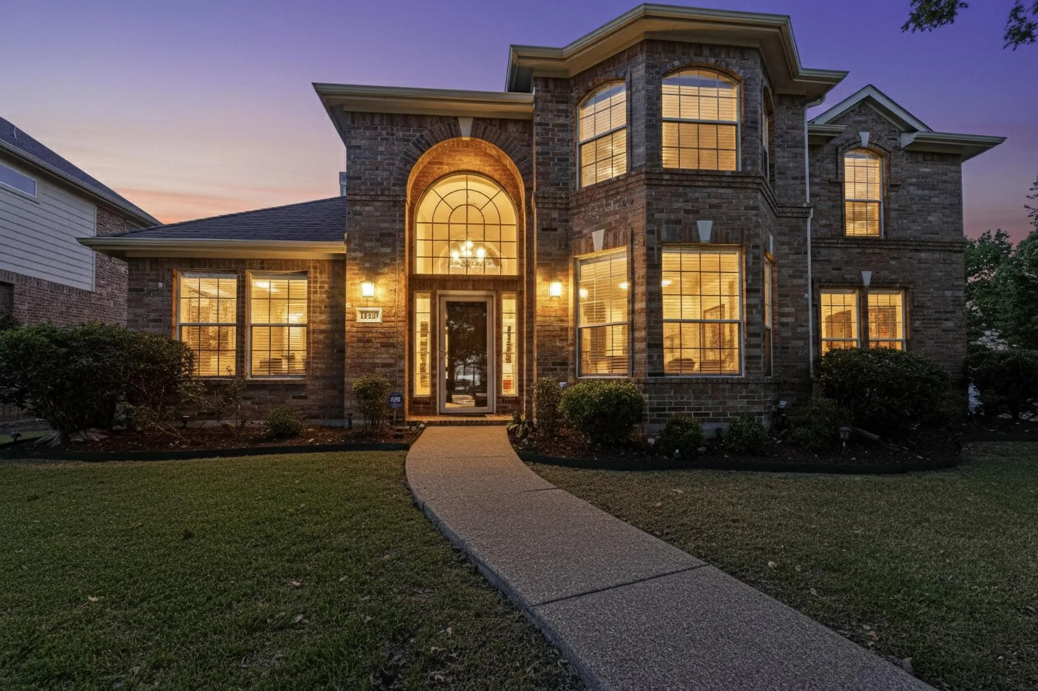 Brick exterior with a prominent arched entry, two-story bay window, and a concrete pathway