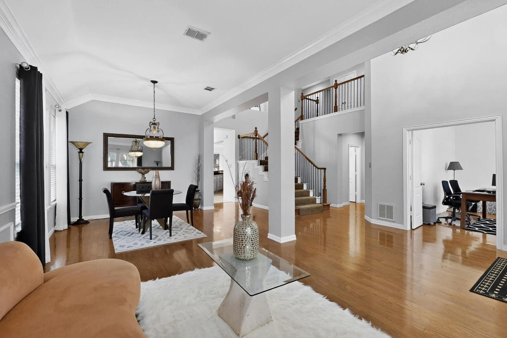 Open-concept living space featuring wood-finish flooring, a formal dining area with chandelier, a two-story entryway, and a carpeted staircase with wood and iron railings