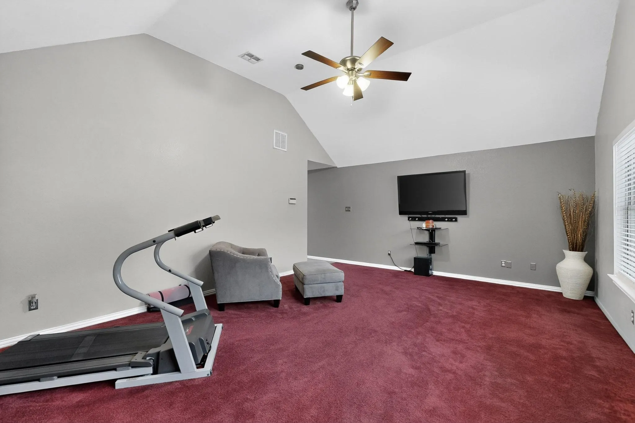 Spacious room featuring vaulted ceilings, a ceiling fan, plush red carpeting, and a wall-mounted entertainment setup