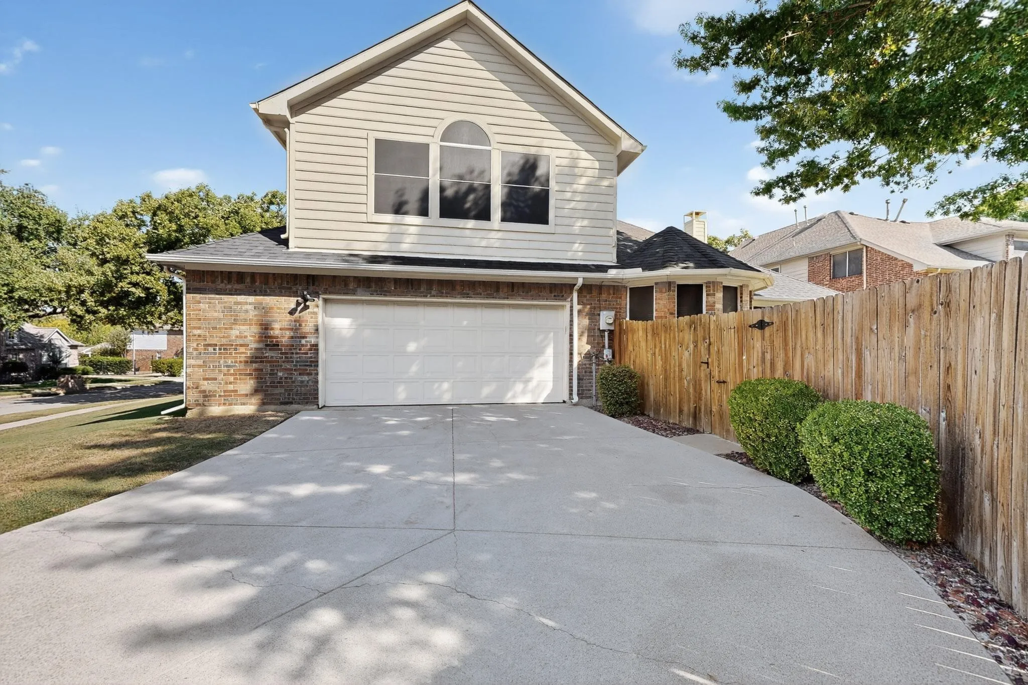 Front exterior featuring a concrete driveway, two-car garage, brick facade, horizontal siding, and an arched window