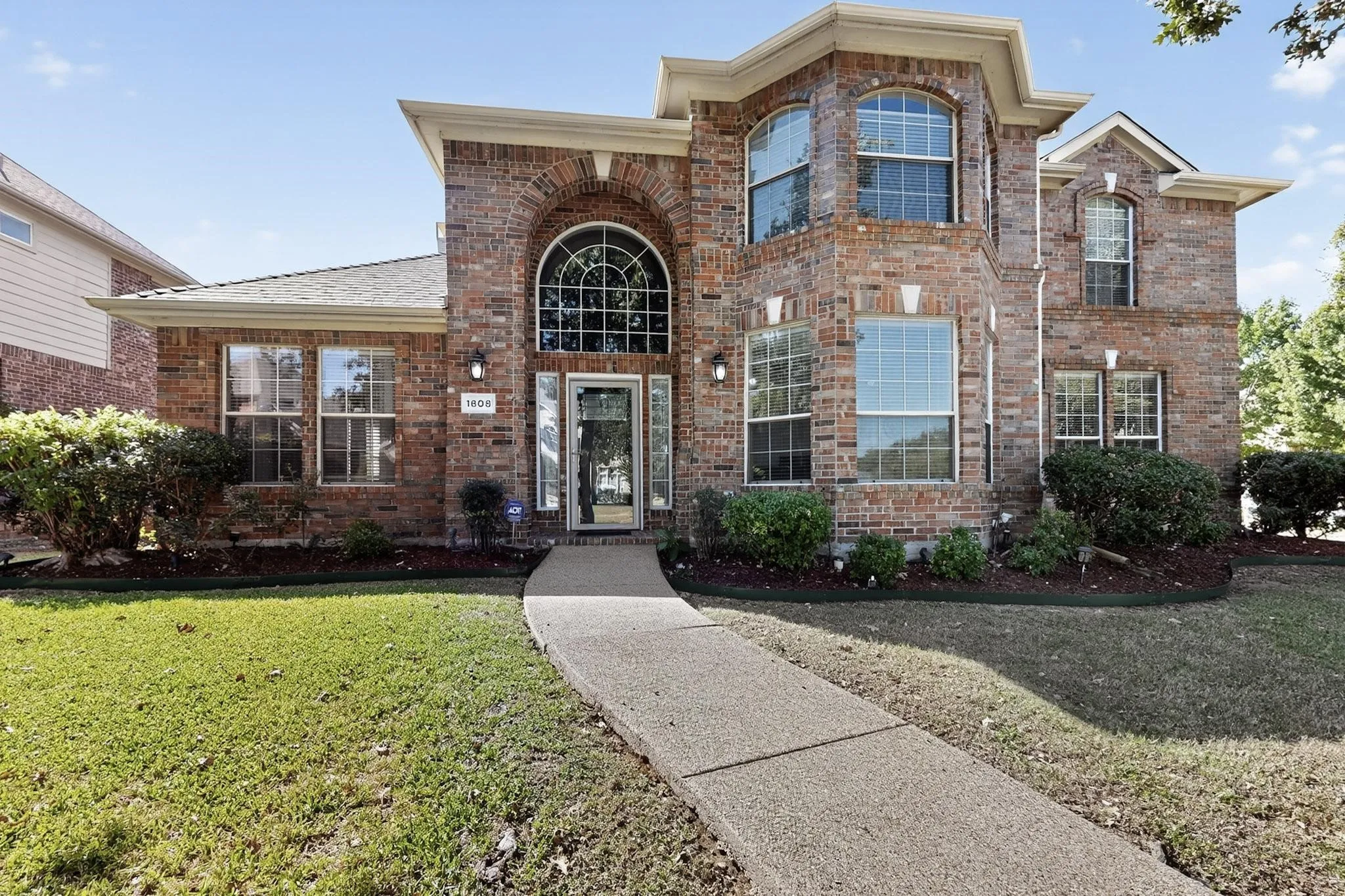 Brick exterior featuring arched windows, multiple large windows, a prominent entryway, and mature landscaping