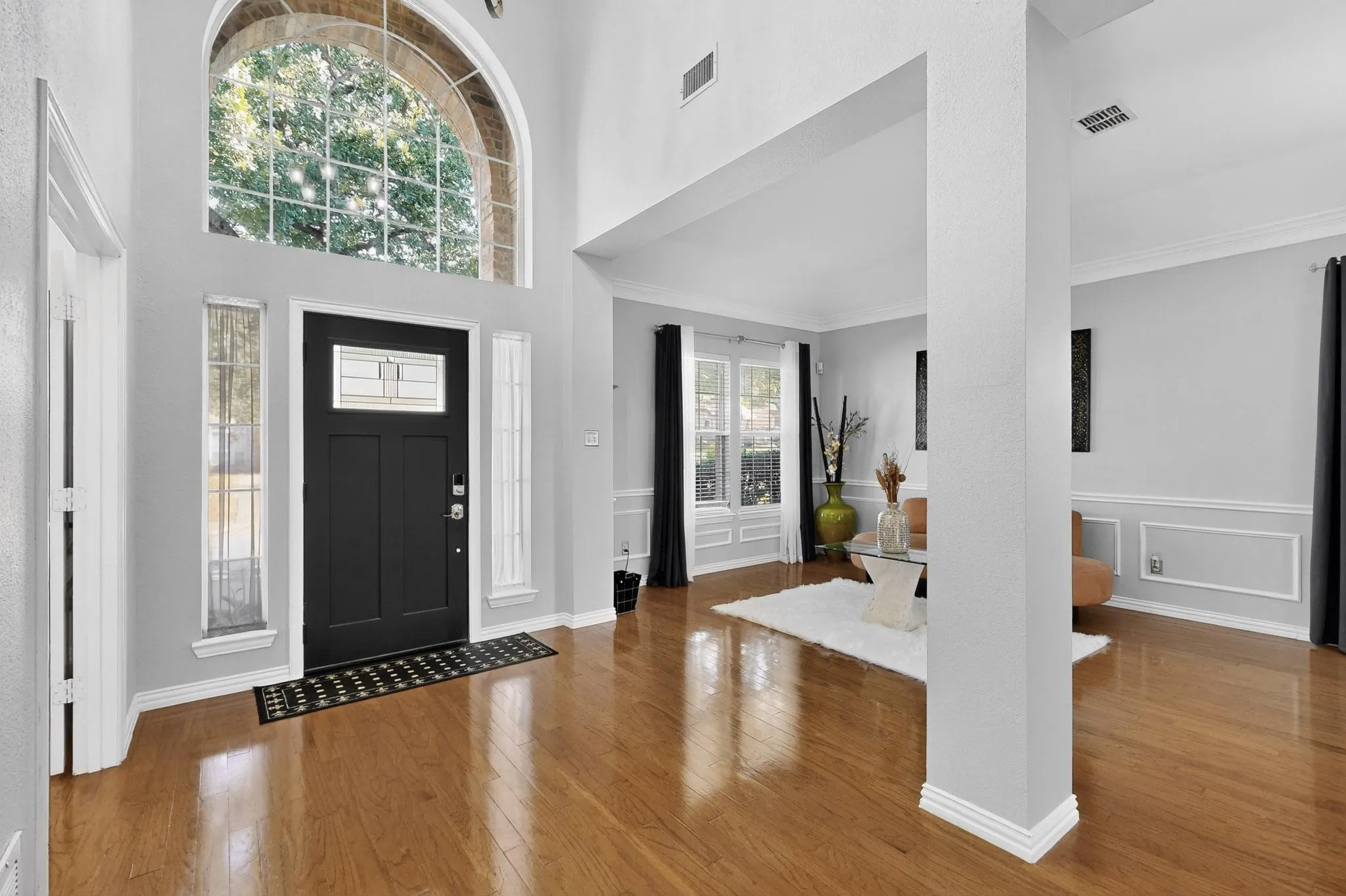 Grand entry featuring a black panel door with leaded glass, an arched transom window, and wood-finish flooring