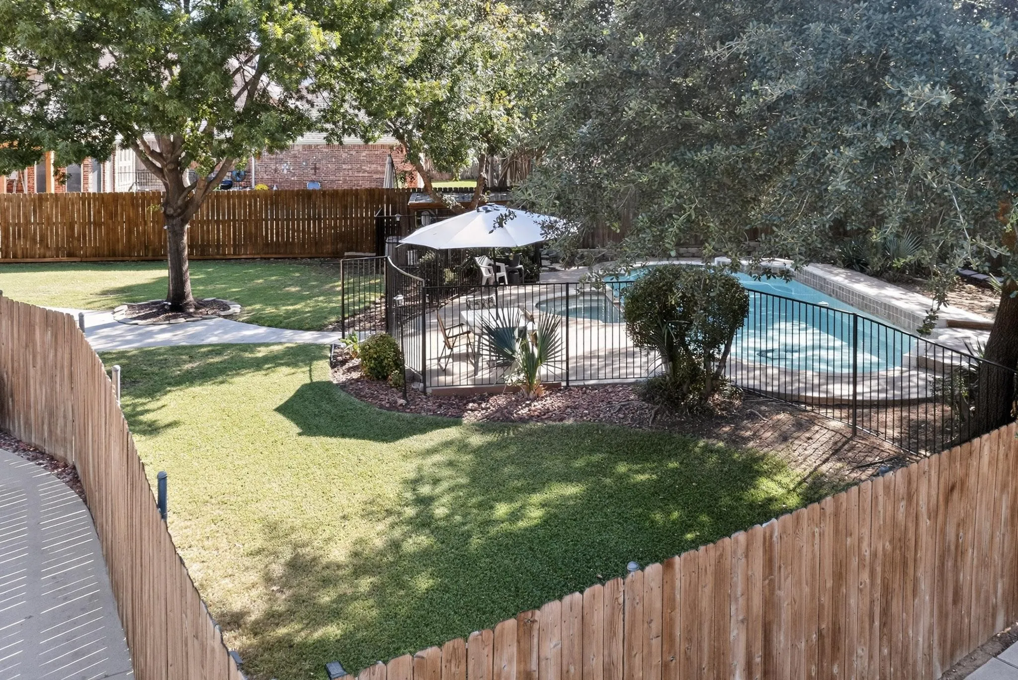 Private backyard featuring an in-ground swimming pool with stone coping, surrounded by a black wrought iron fence