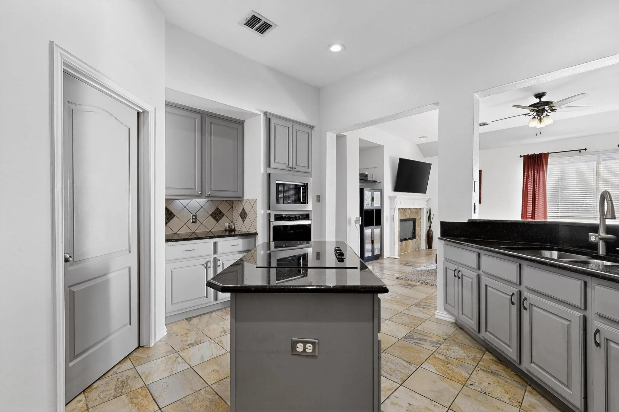 Kitchen featuring gray cabinetry, black countertops, stainless steel built-in appliances, a central island with an integrated cooktop, and tile flooring