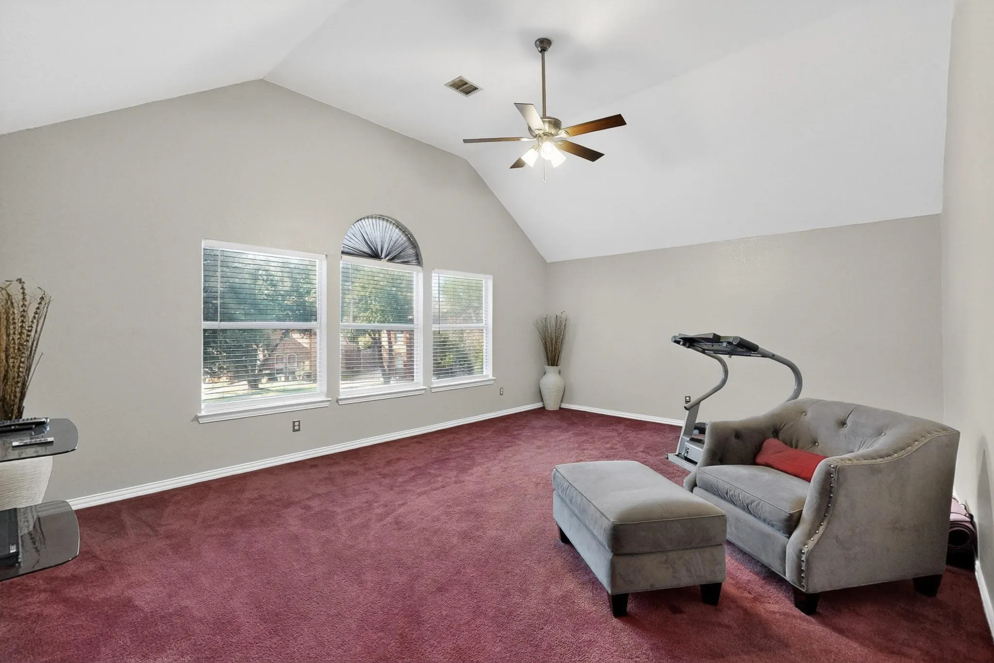 Vaulted ceiling room featuring a ceiling fan with light fixture, three windows with blinds, an arched transom window, and red carpeting