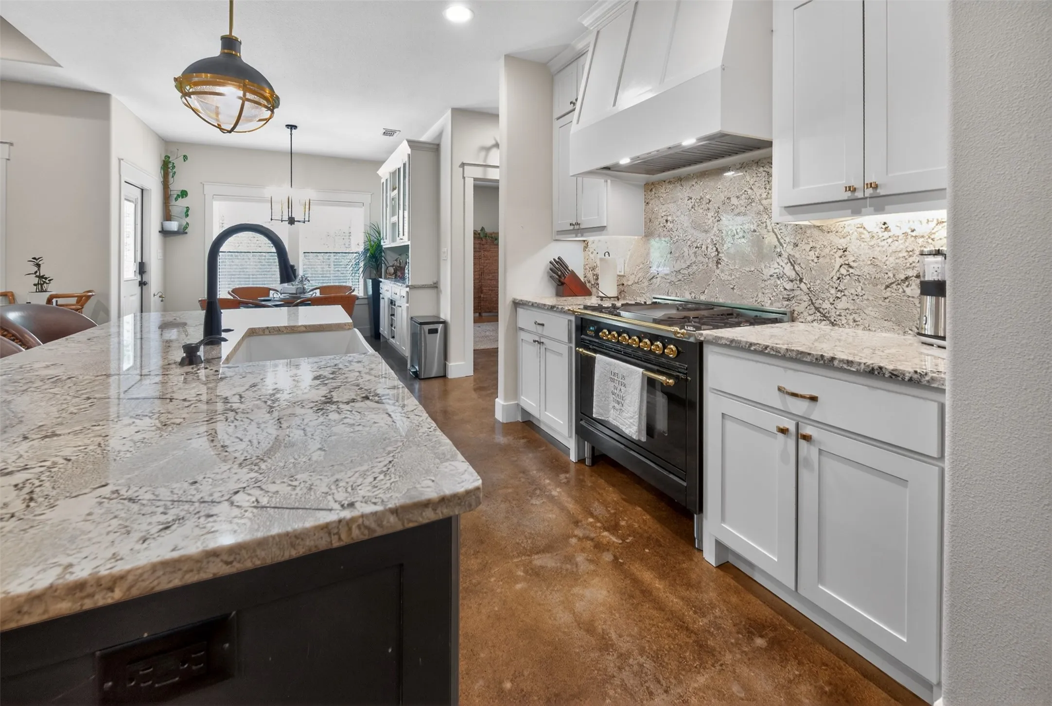The kitchen features an island with a light-colored granite countertop and sink, a black faucet, and white cabinetry
