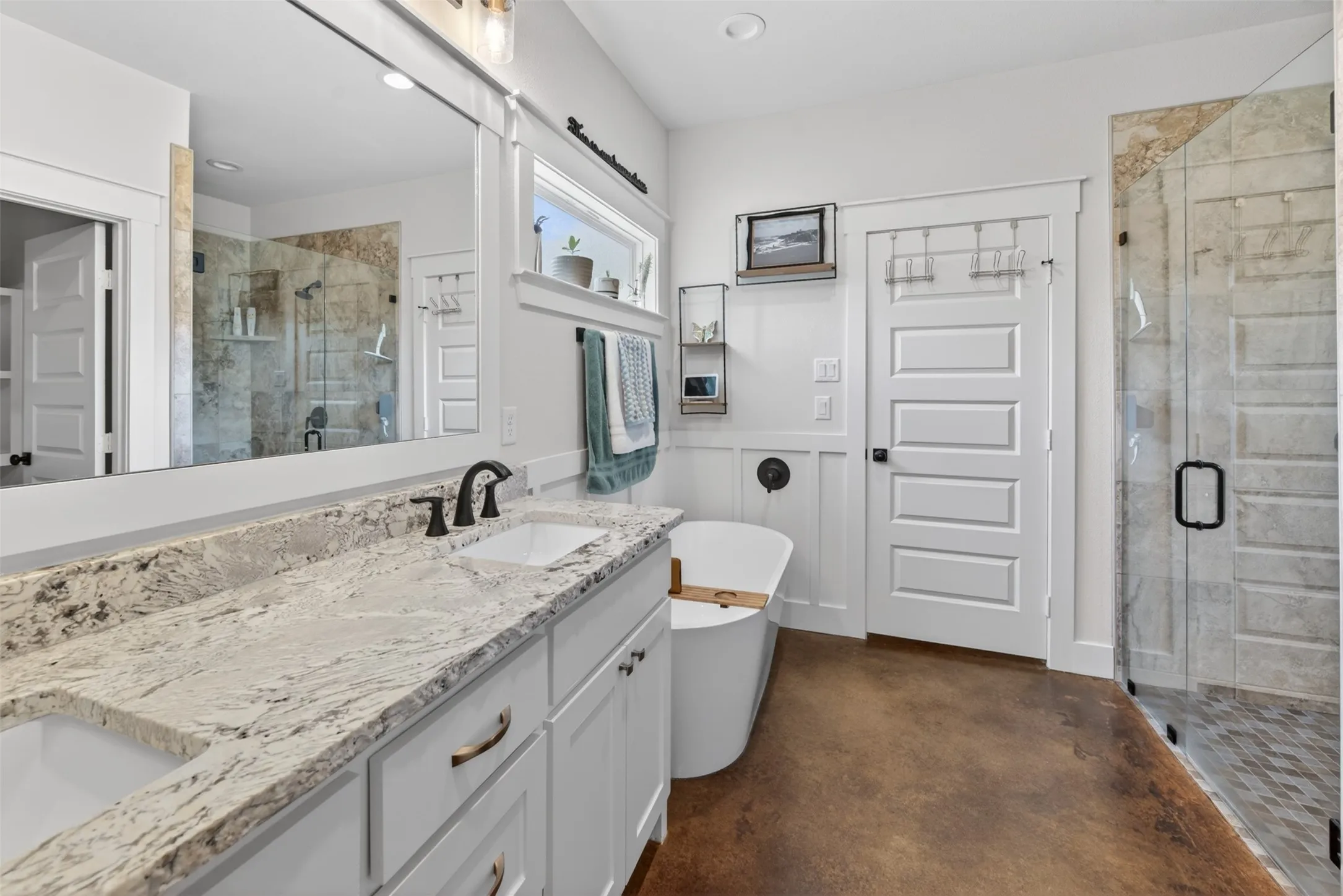 Contemporary bathroom featuring a spacious vanity with a light-toned granite countertop and two sinks, a freestanding soaking tub, and a glass-enclosed shower