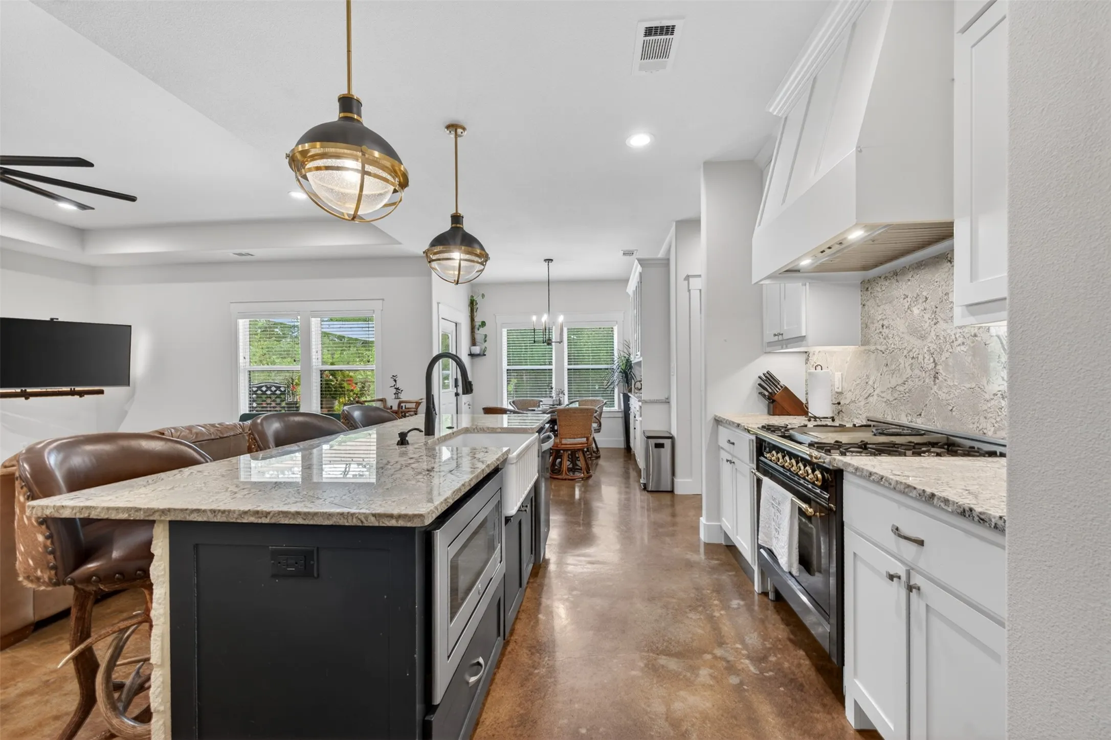 The kitchen features white cabinetry, a large kitchen island with a farmhouse sink, granite countertops, and an ILVE custom commercial range with a matching hood