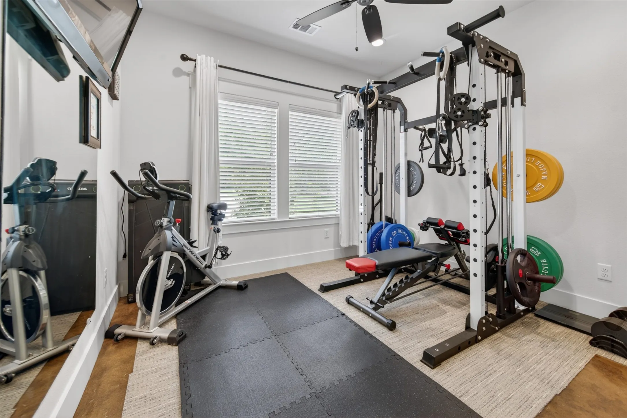 Dedicated fitness area with ample natural light from two windows, featuring a ceiling fan, and a neutral color palette