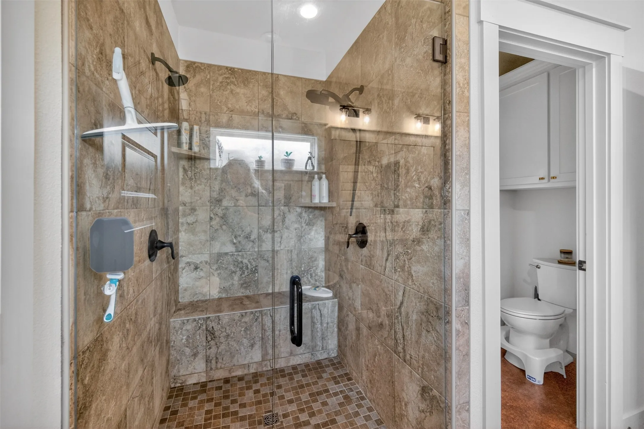 The bathroom features a spacious shower with glass enclosure, tiled walls and floor, built-in shelving, and a shower bench