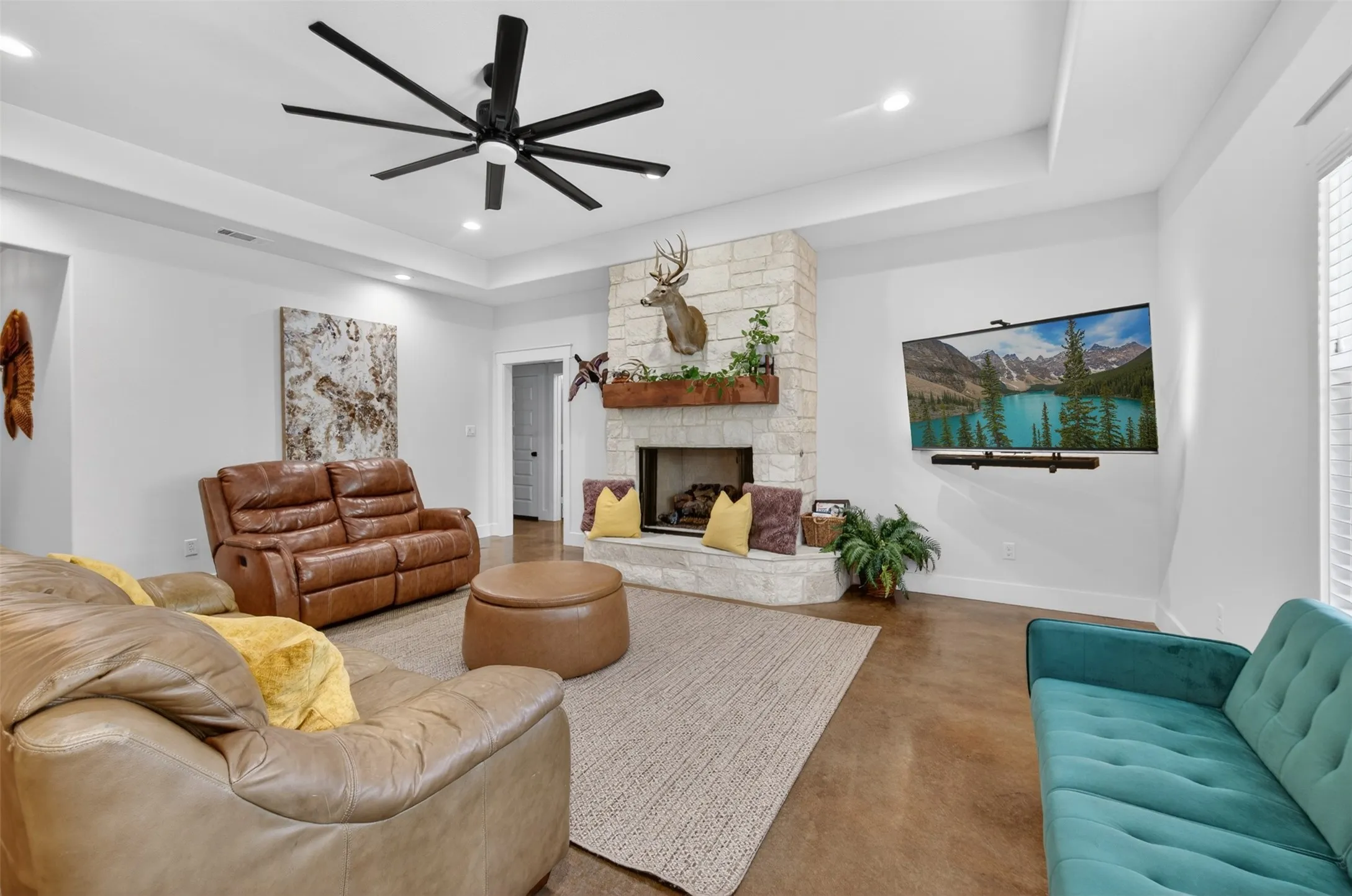 Living area featuring a stone fireplace with a wooden mantel, a large ceiling fan, and recessed lighting