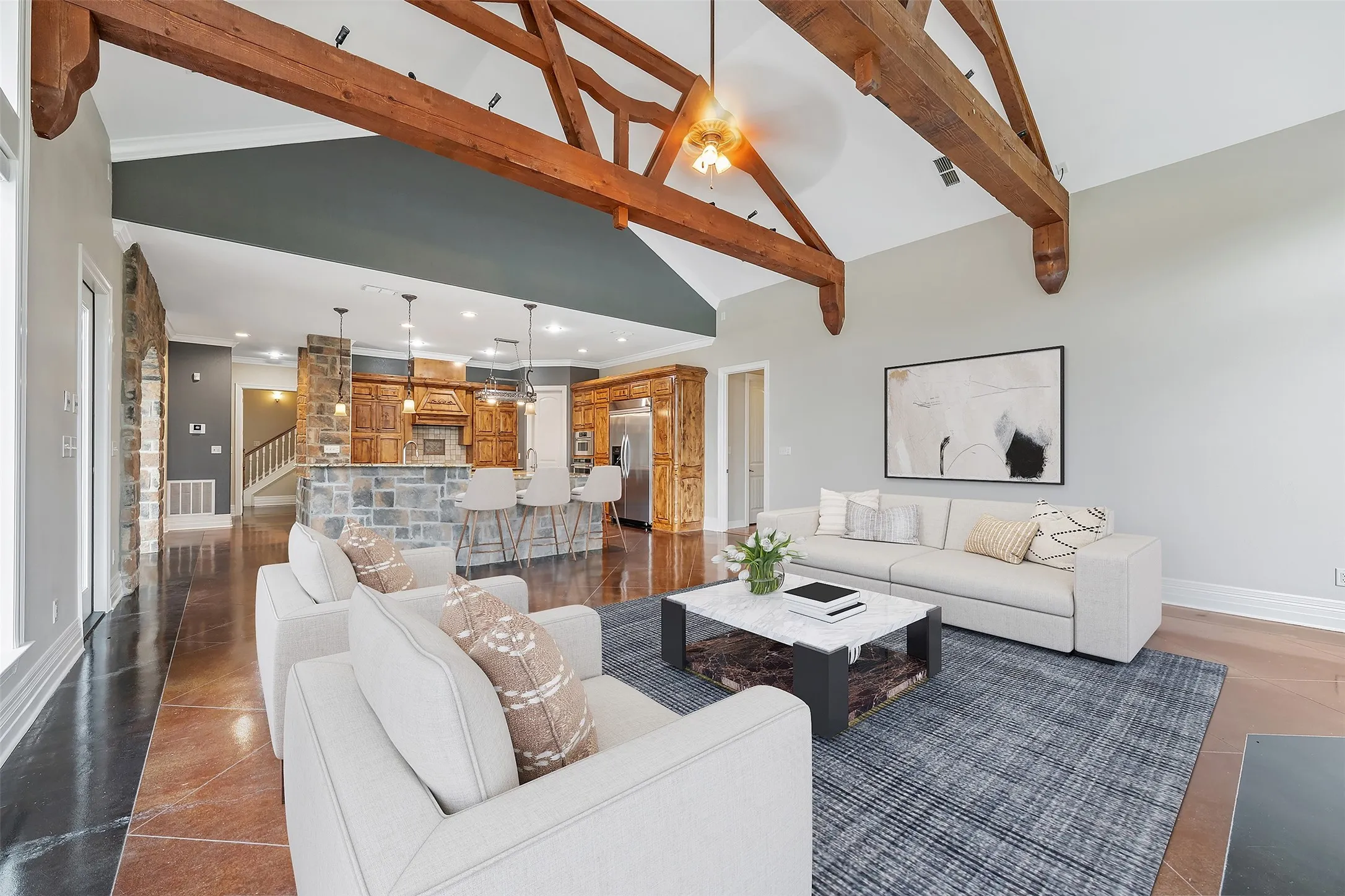 Vaulted ceiling with exposed wood beams, stone accent walls, and an open-concept layout