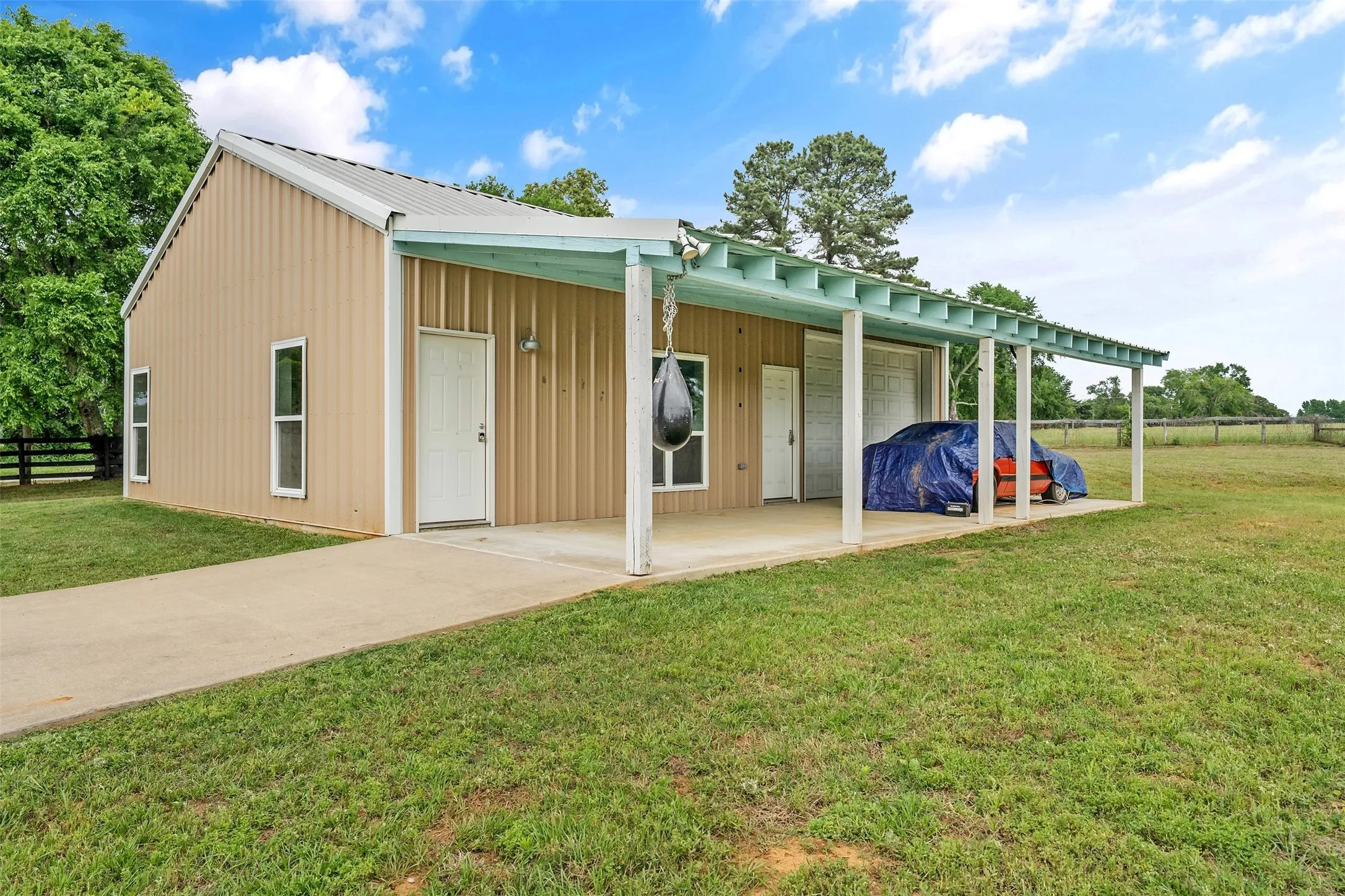 Metal-sided building featuring a covered porch, concrete drive, multiple windows, and a roll-up door