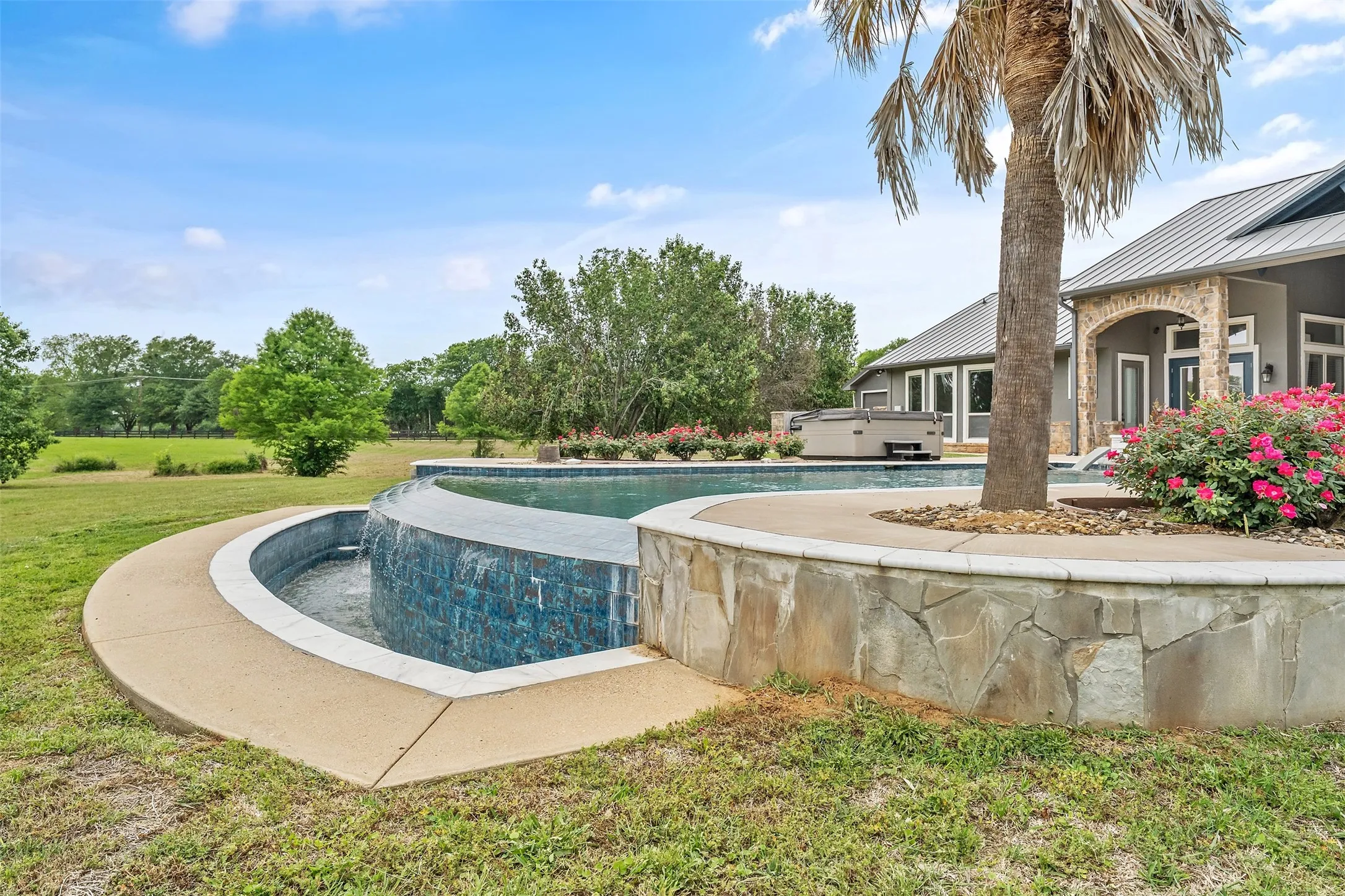Resort-style pool with a waterfall feature, stone-clad retaining wall, and integrated hot tub