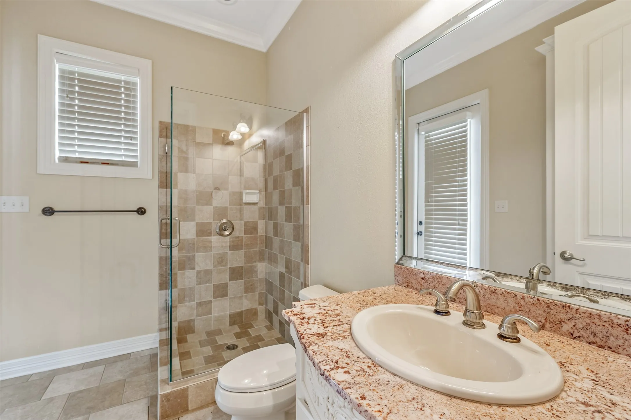 Bathroom featuring a glass-enclosed shower with tiled walls and flooring, a single vanity with a stone countertop, an oval undermount sink, and a framed wall mirror